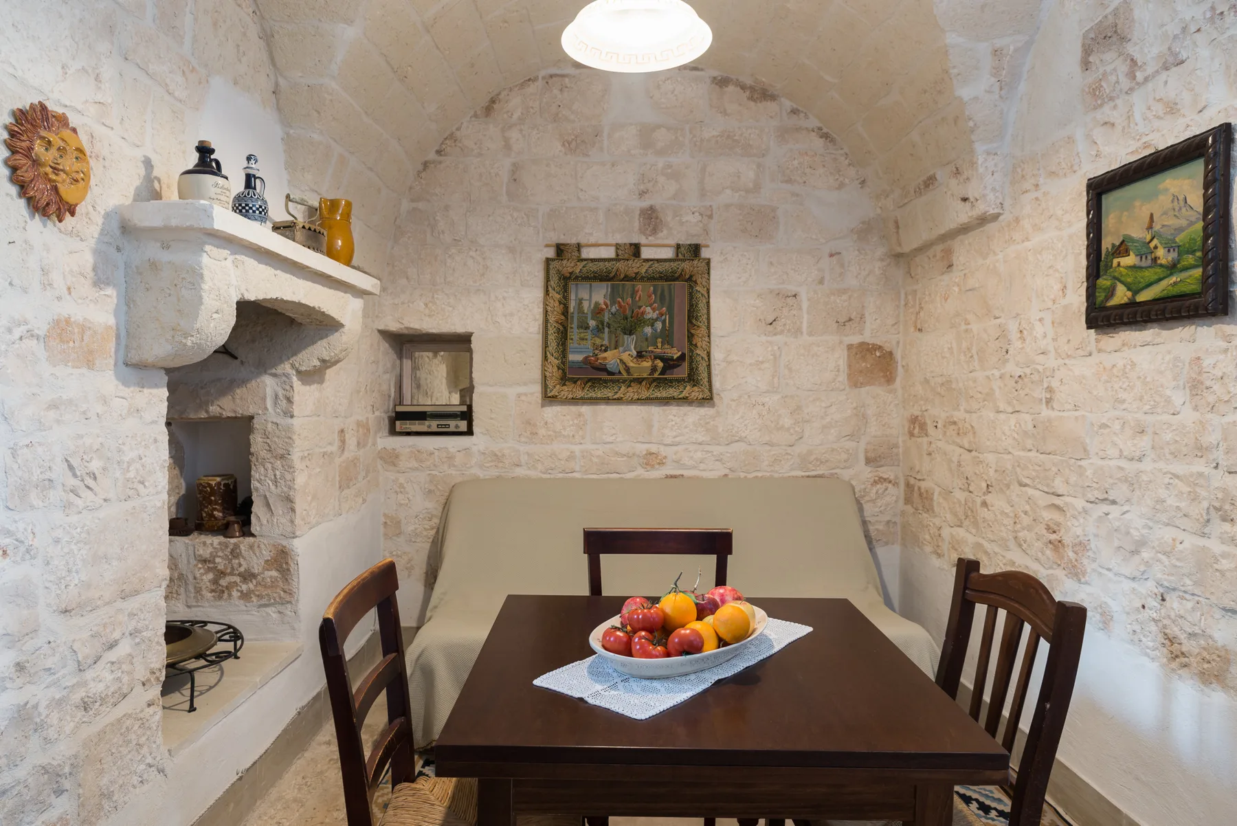 A stone dining room with a wooden table, chairs, and a bowl of fruit.