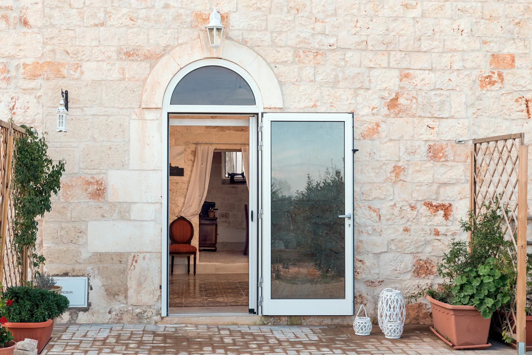 A stone building entrance with an open glass door and potted plants.