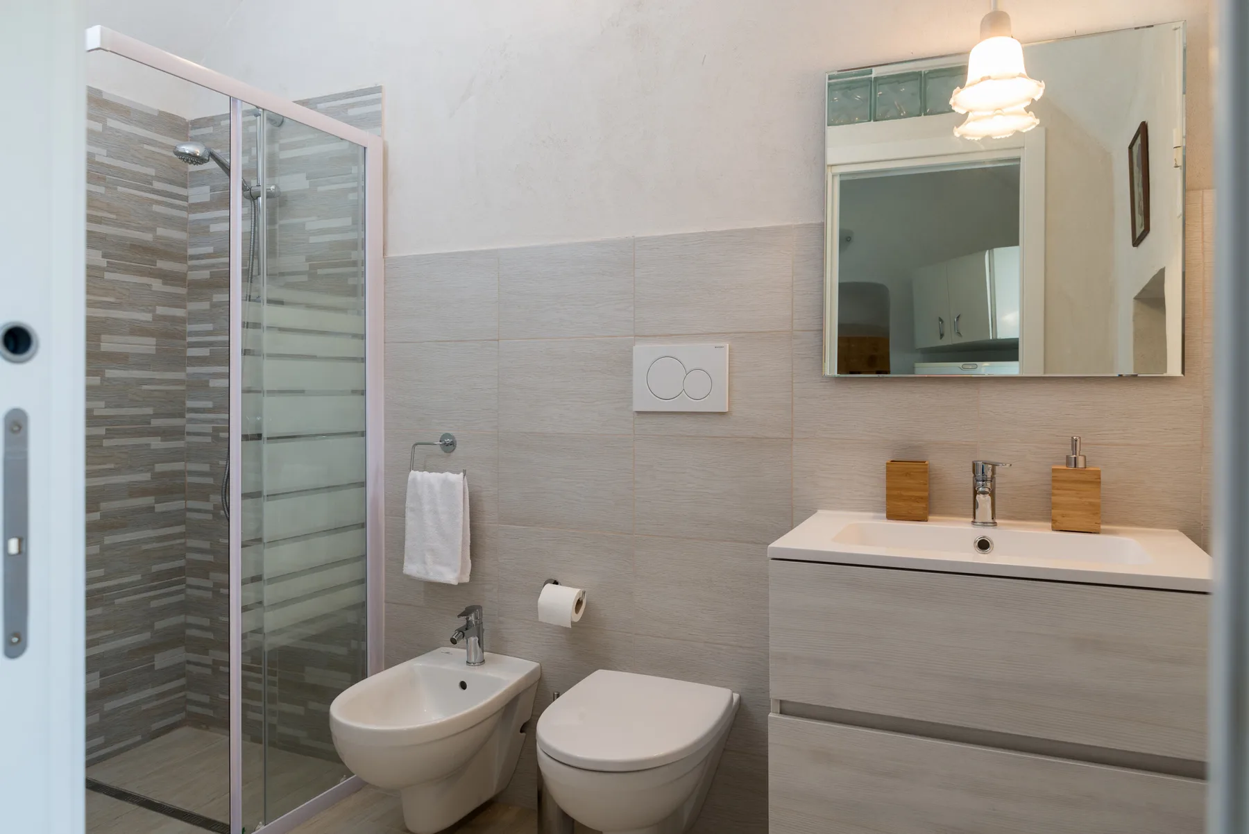 A tiled bathroom with a glass shower, sink, bidet, and toilet.
