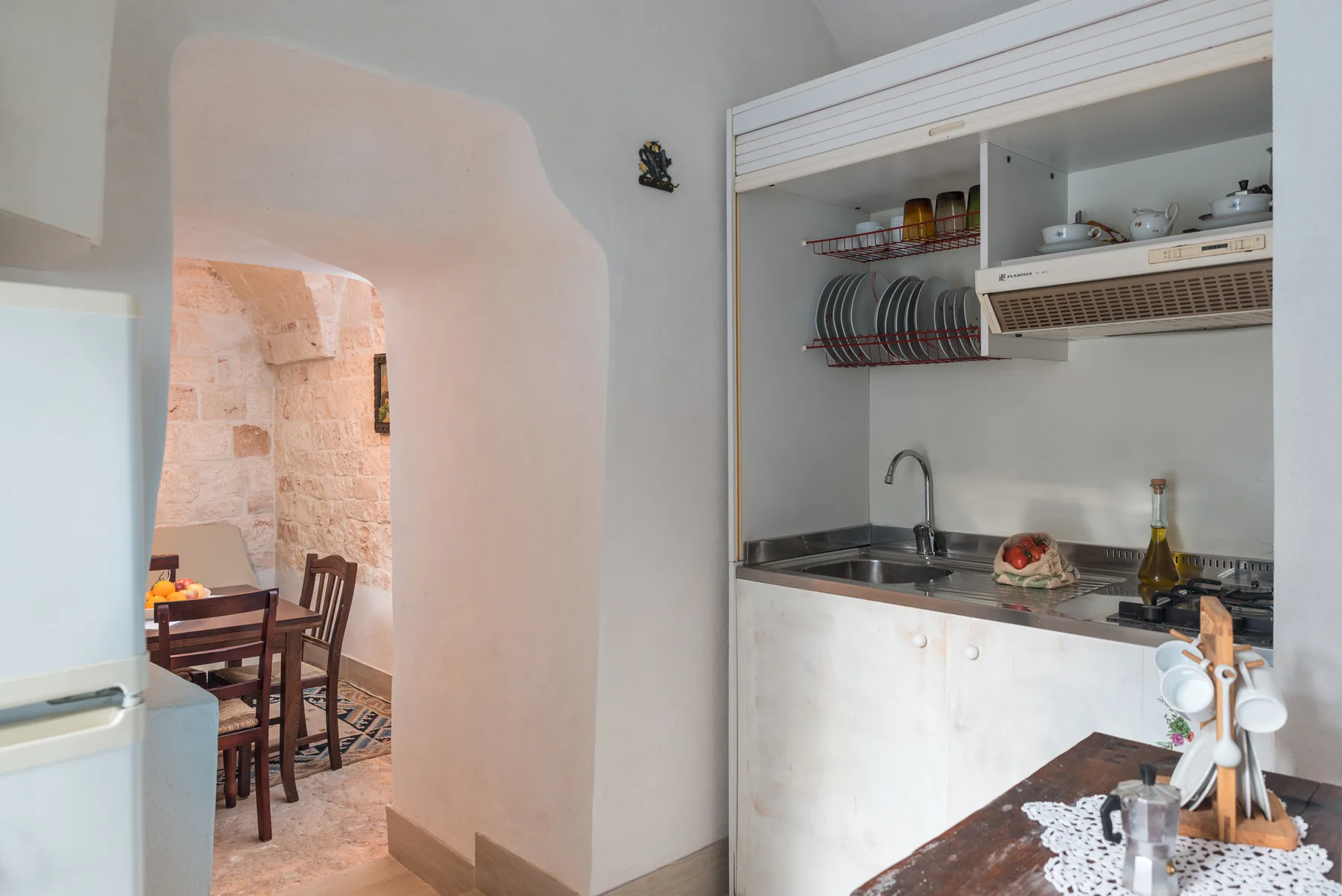 A kitchen with a sink and dish rack beside an arched opening to a dining area.