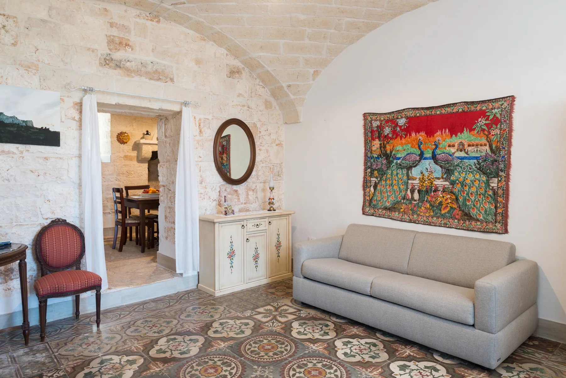 A sitting room with a light-colored sofa beneath a colorful wall tapestry.