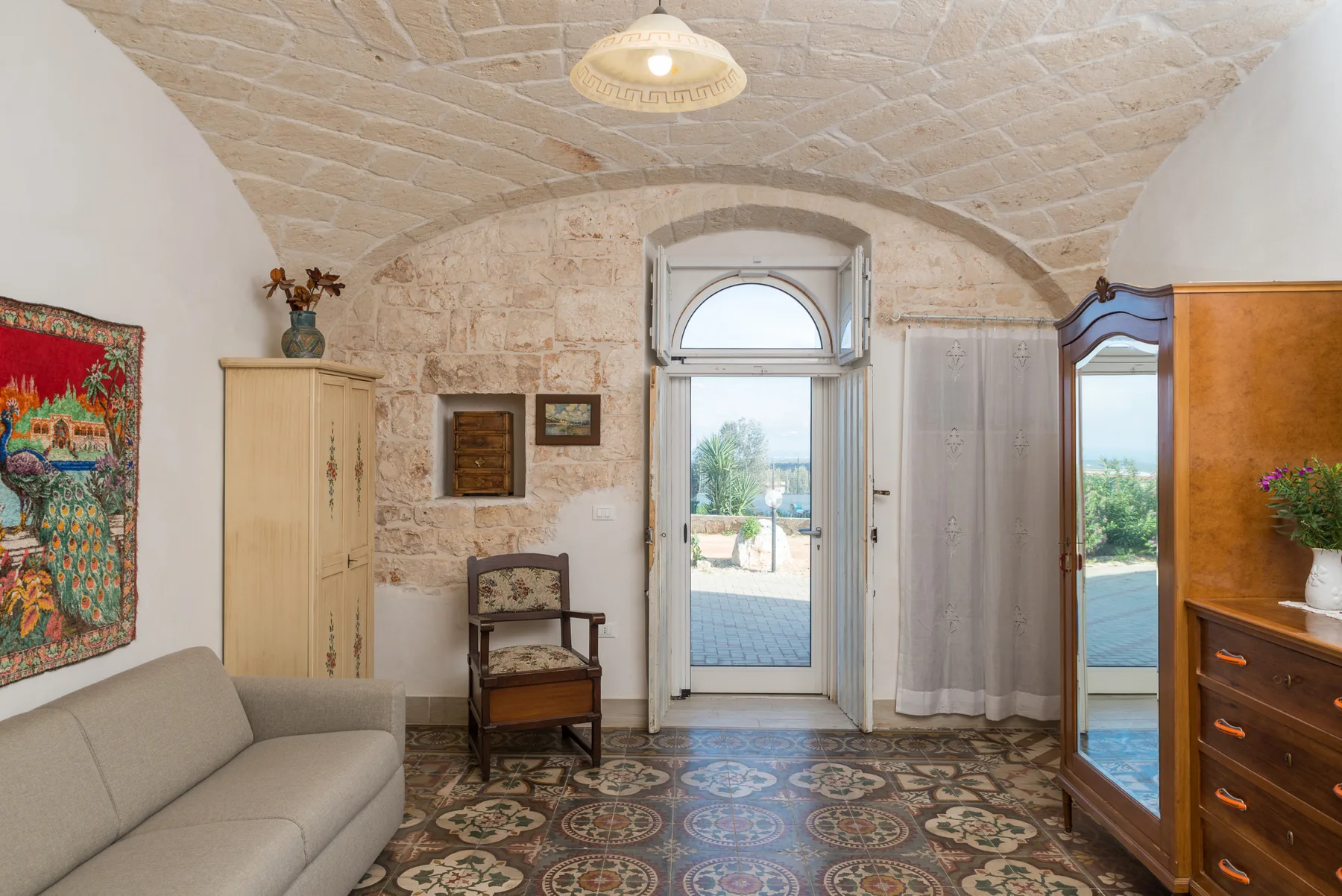A vaulted bedroom with a bed, patterned floor tiles, and a glass door.