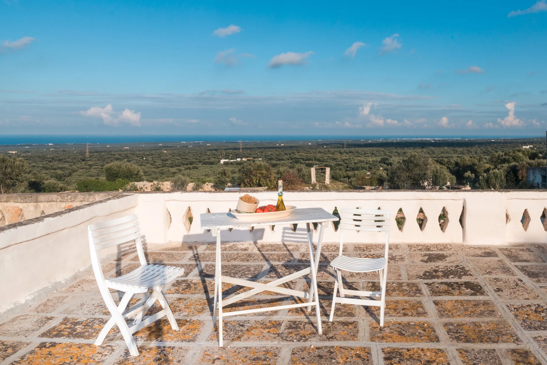 A rooftop terrace has a white table and seating overlooking a broad landscape.