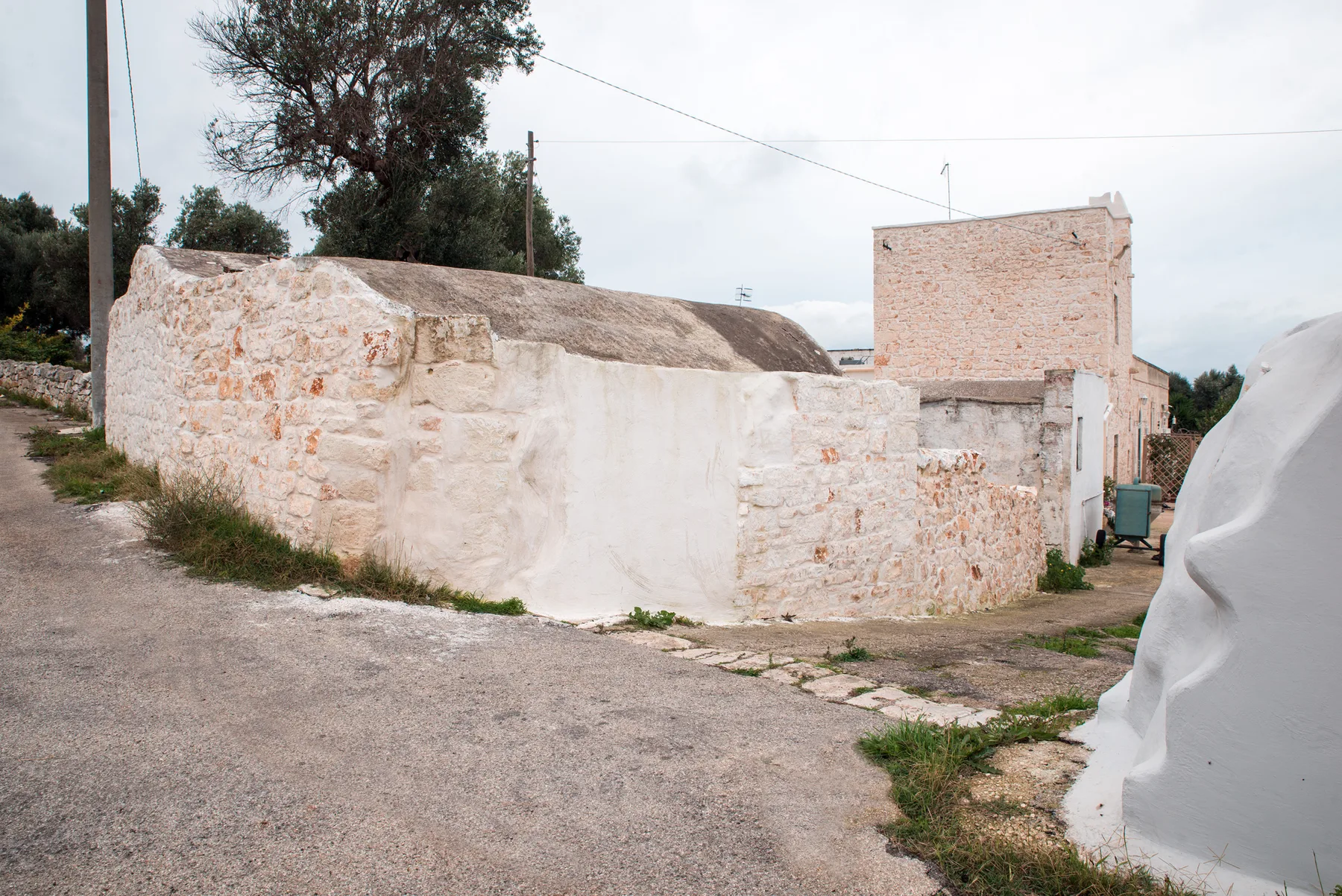 A narrow paved lane runs beside a low stone wall and pale buildings.
