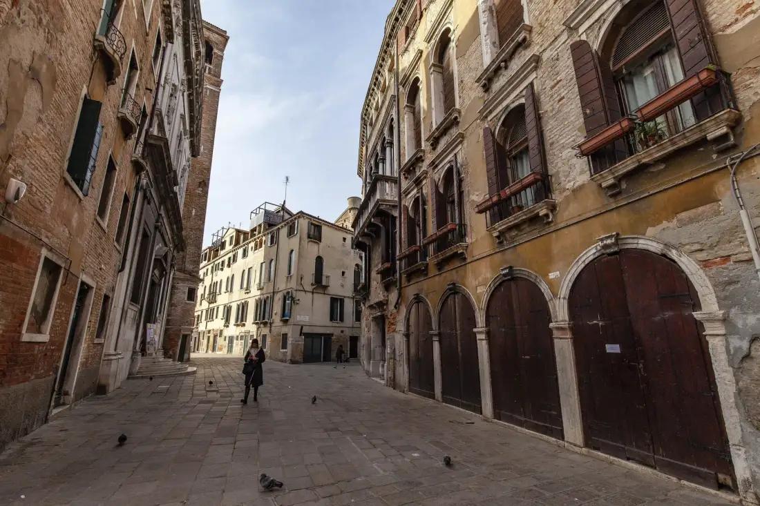 A narrow stone-paved street runs between old multi-story buildings with arched entrances.