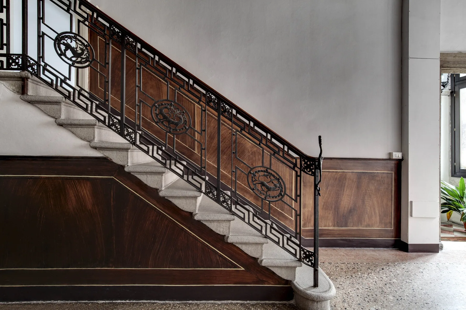 An indoor staircase with decorative metal railings descends beside a wood-paneled wall.