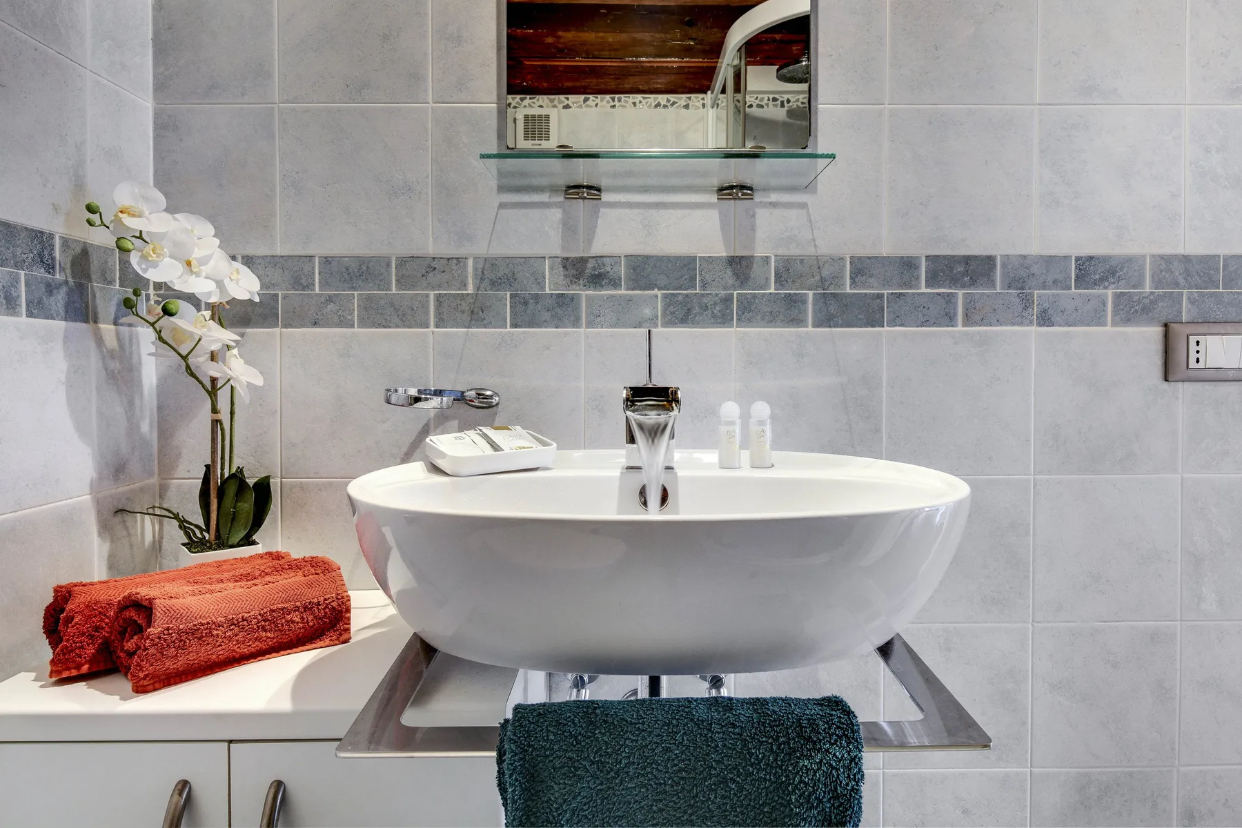 A bathroom vanity features a white vessel sink, wall mirror, and folded towels.