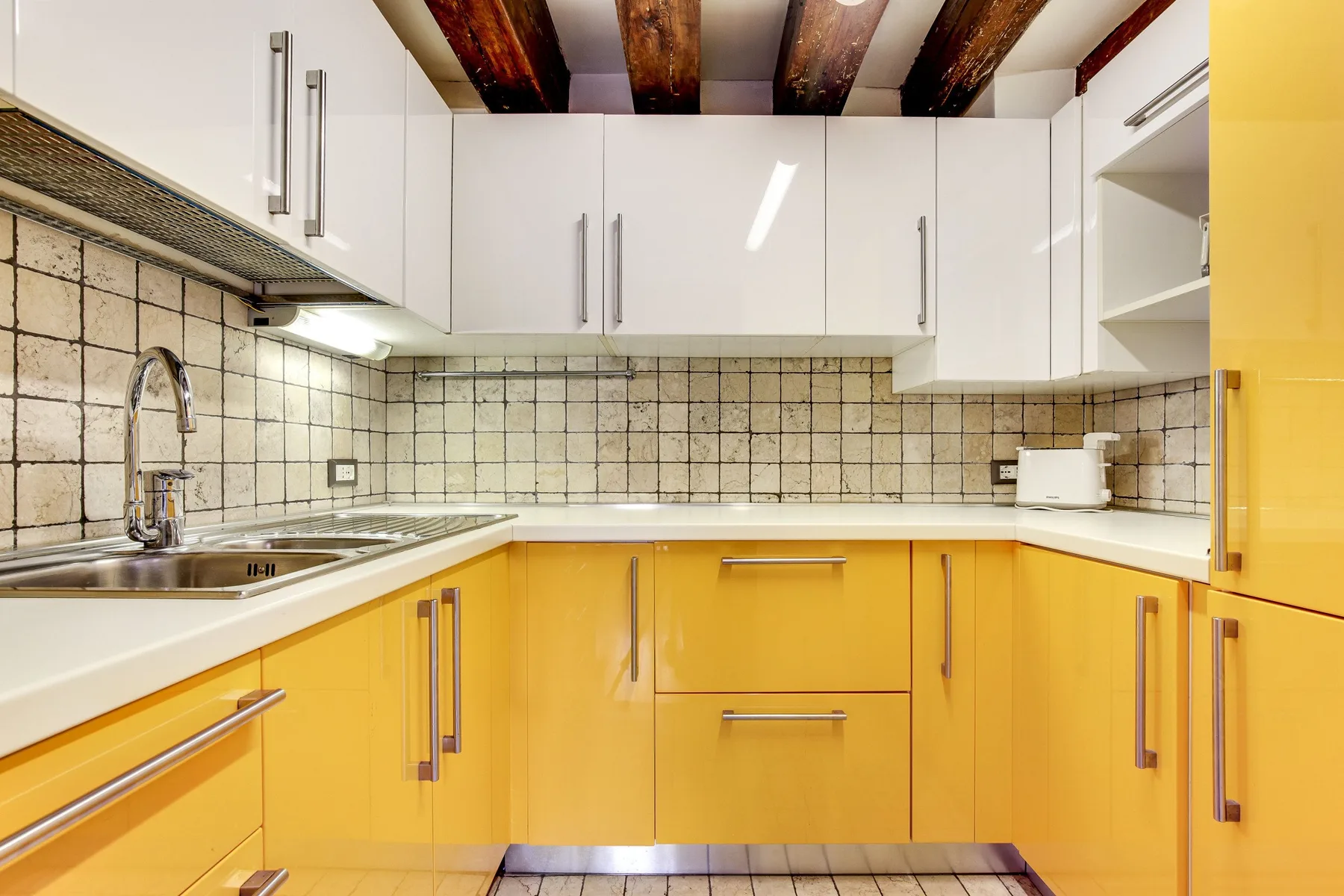 A bright kitchen with white upper cabinets, yellow lower cabinets, and a tiled backsplash.