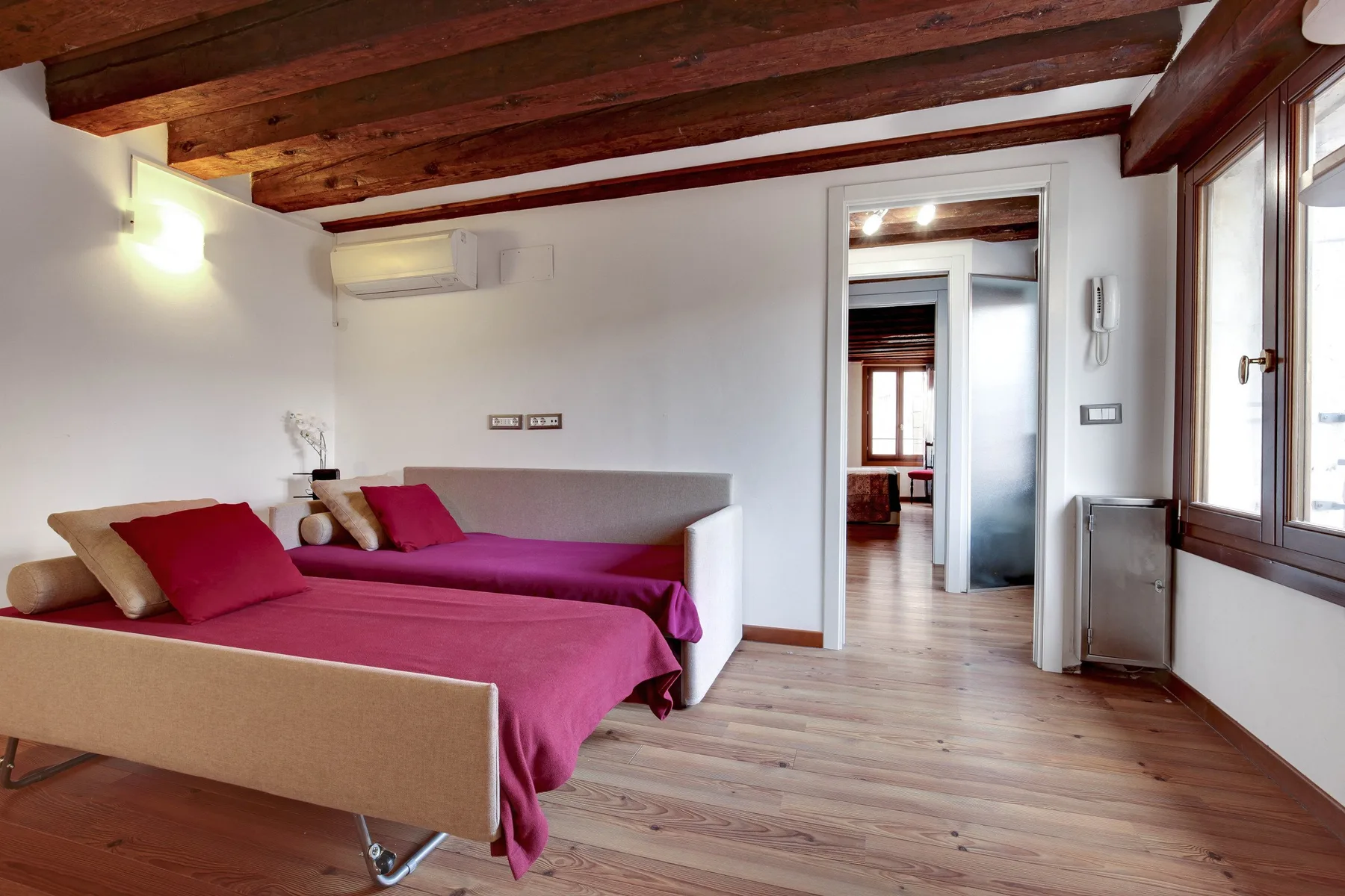 A bedroom with two beds covered in magenta bedspreads and a wood-beam ceiling.