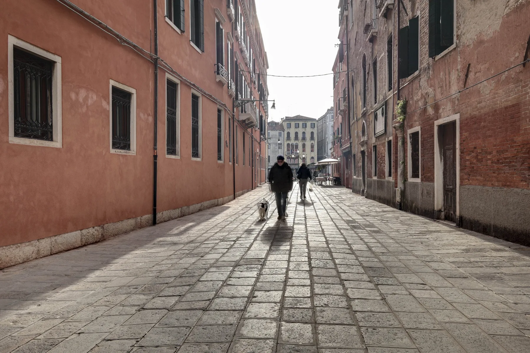A narrow paved street runs between rows of old buildings, with pedestrians walking through.