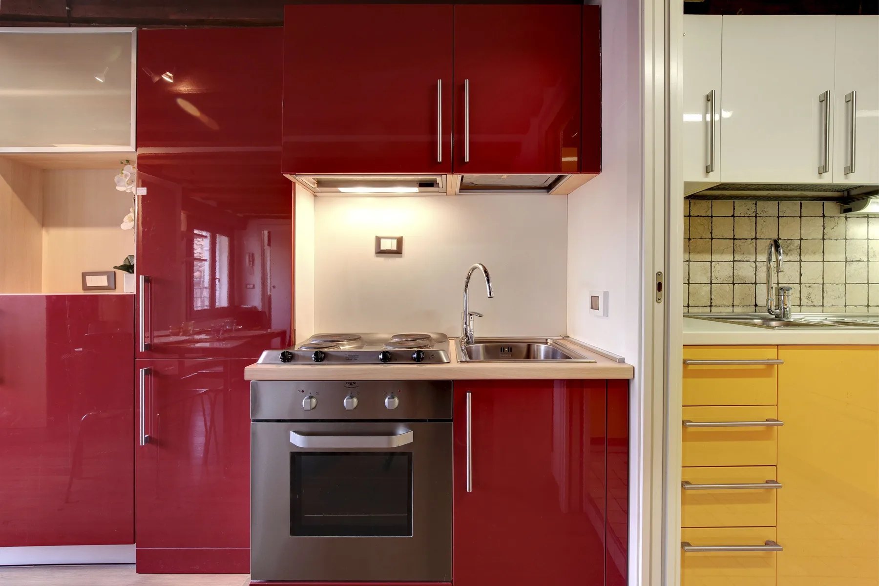 A modern kitchen with red cabinets, a cooktop, oven, and sink.