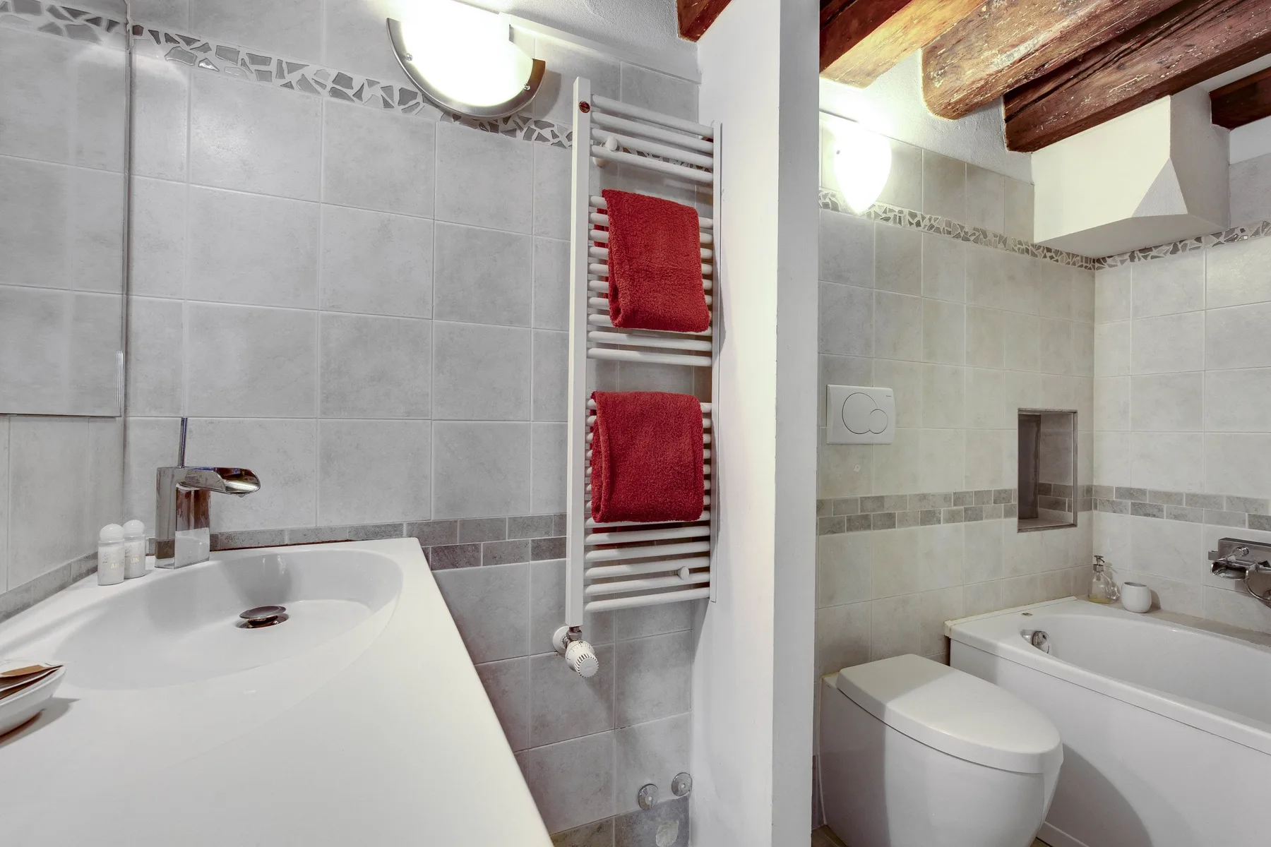A tiled bathroom with a bathtub, toilet, and red towels on a heated rail.