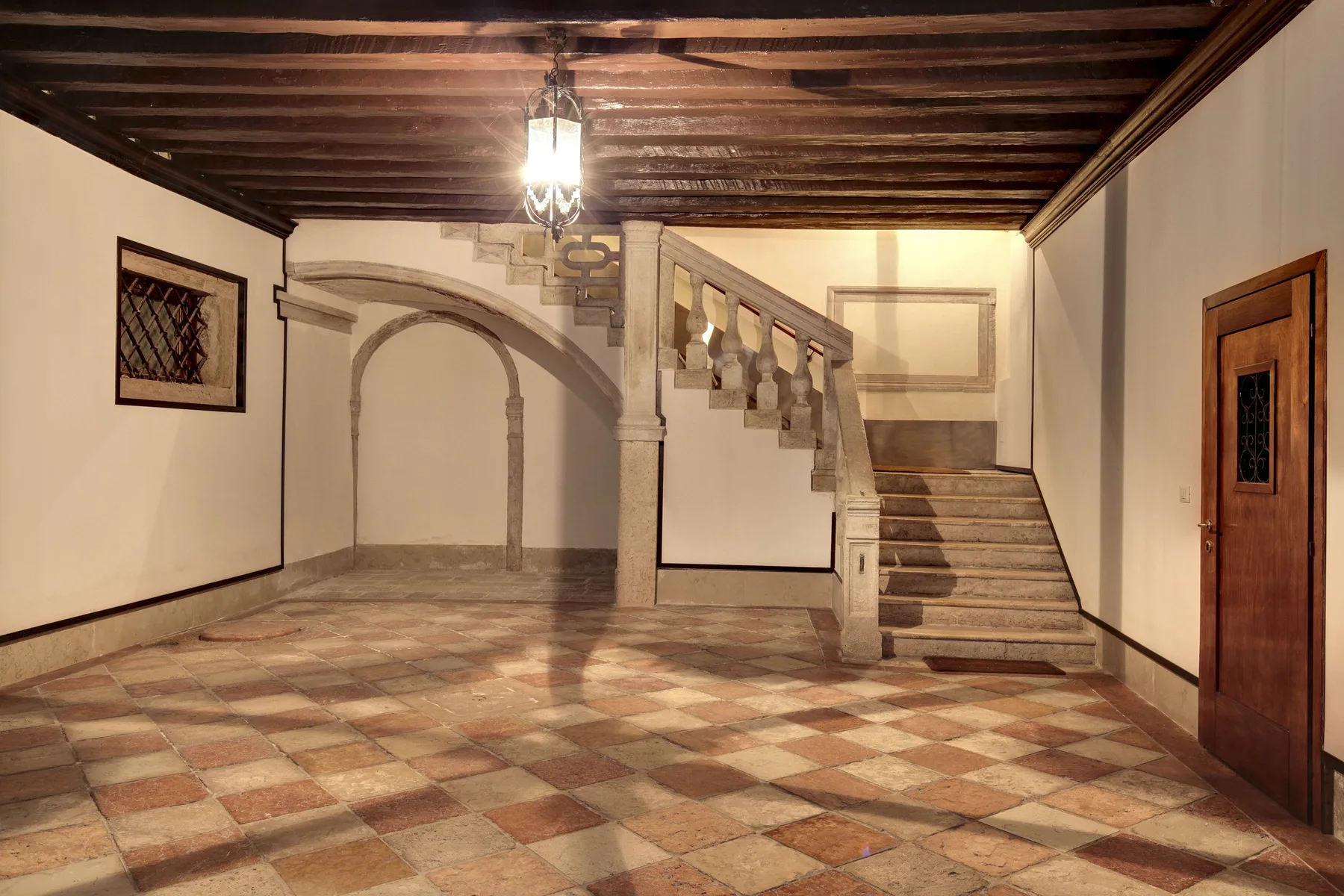 An interior hallway with a staircase, arched alcove, and patterned tile floor.