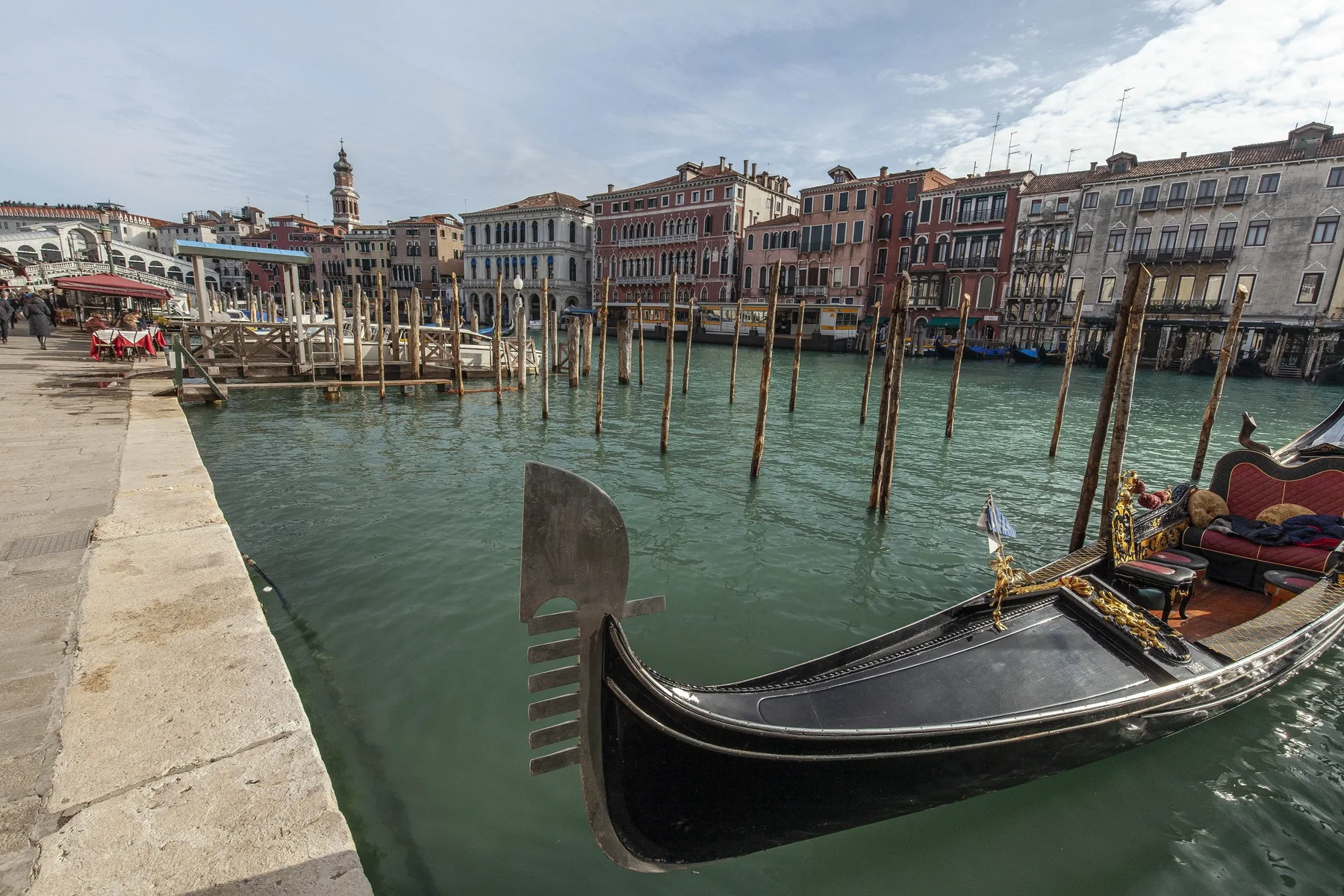 A gondola floats in a canal lined with historic buildings and wooden mooring poles.