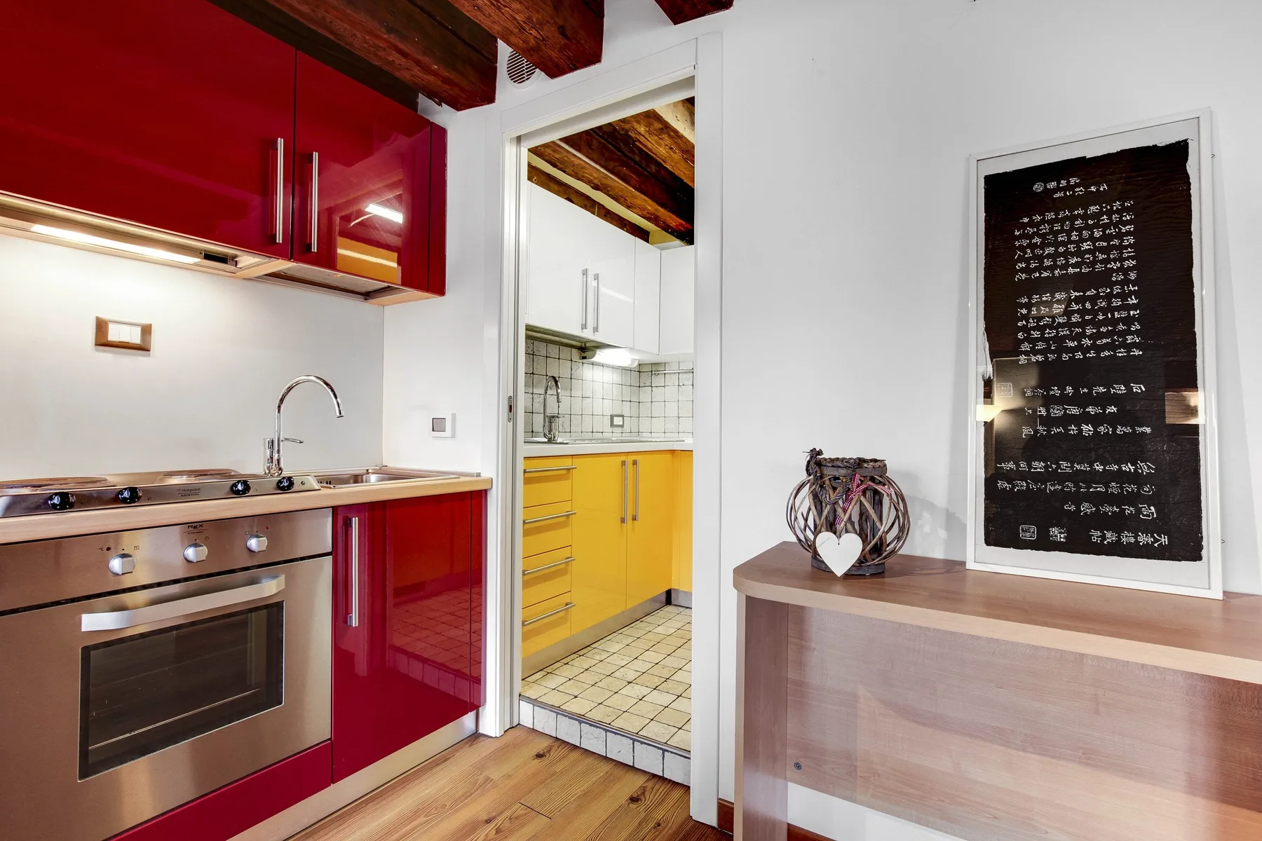 A compact kitchen with red cabinets, yellow drawers, and a tiled backsplash.