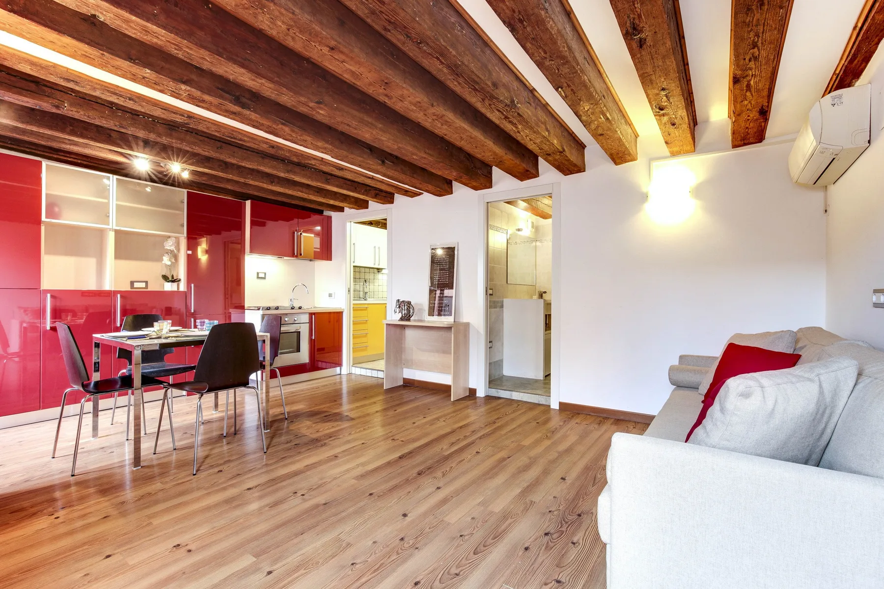 An open-plan living area with a red kitchen, dining table, and seating.
