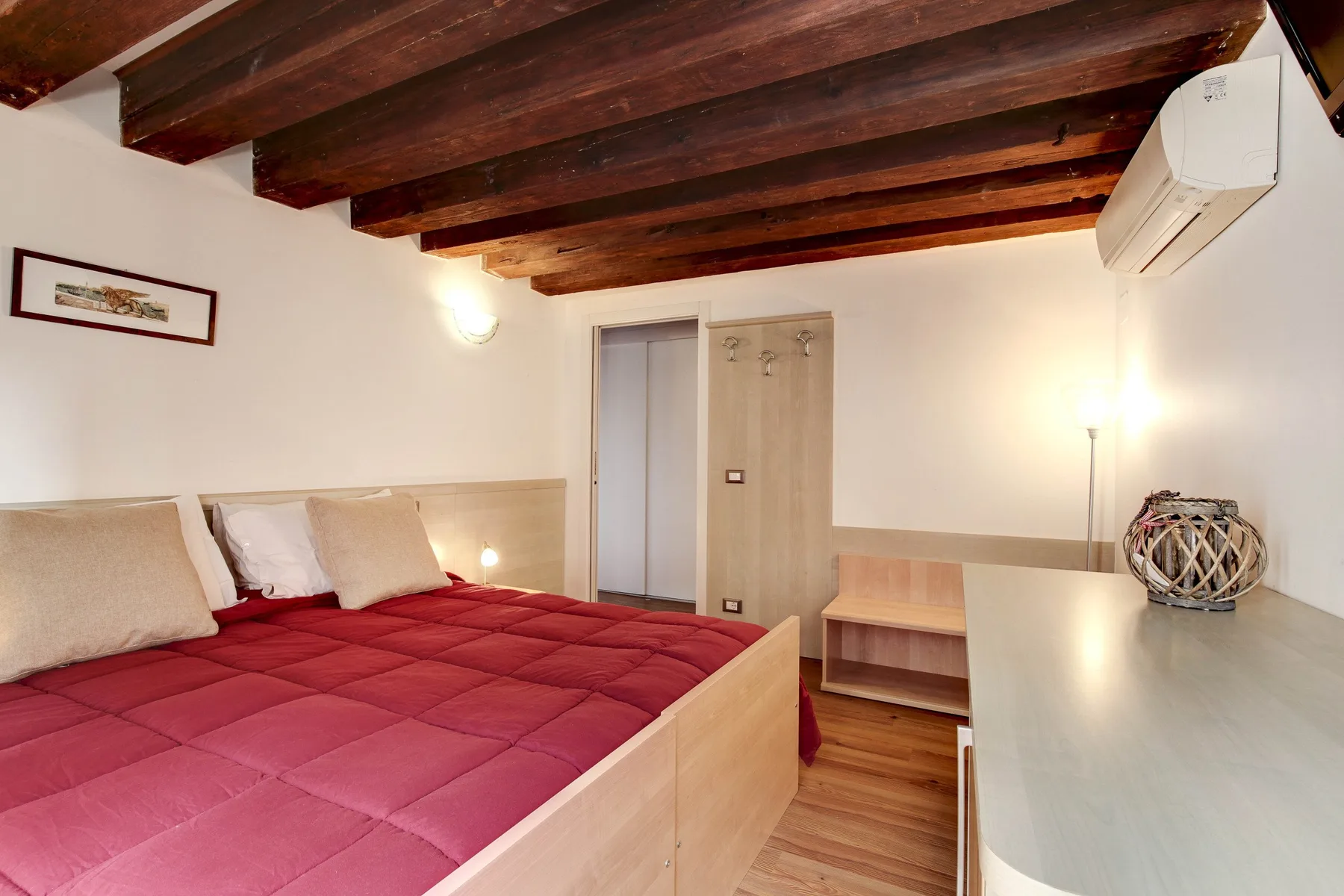 A bedroom with a red bed, a wooden ceiling, and a desk.