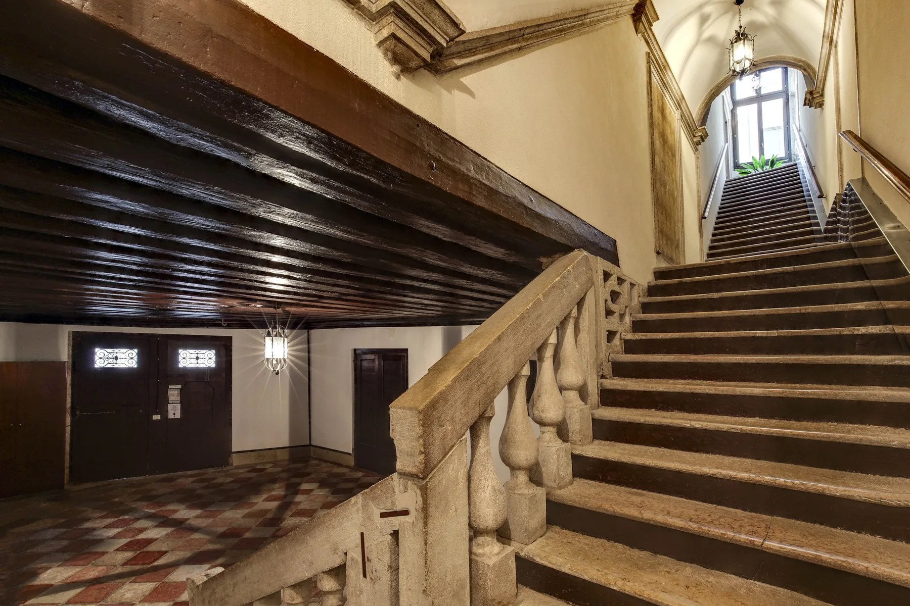 A grand interior staircase rises toward a tall arched window.