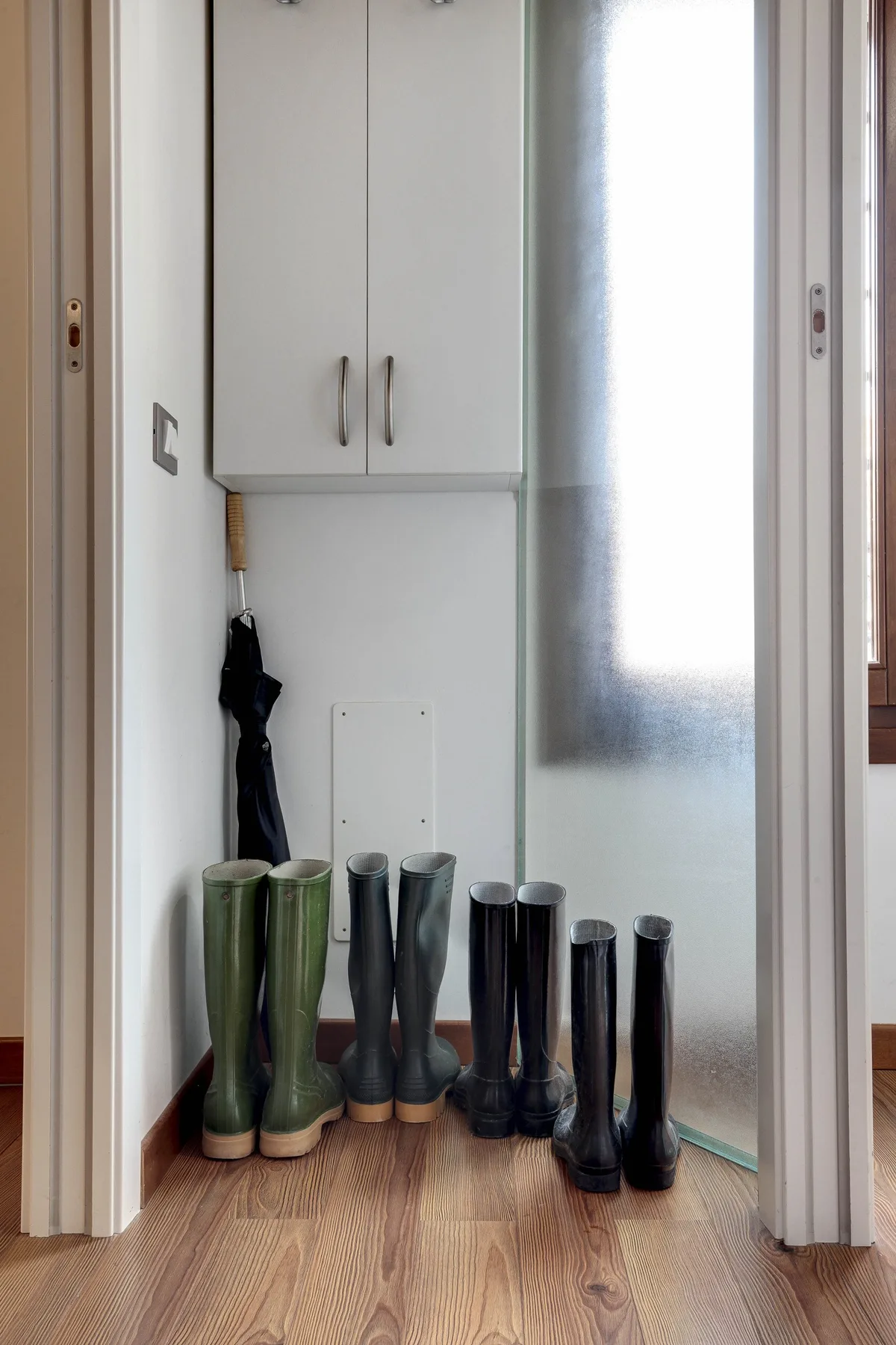 A narrow entryway with rain boots lined up beneath a wall cabinet.