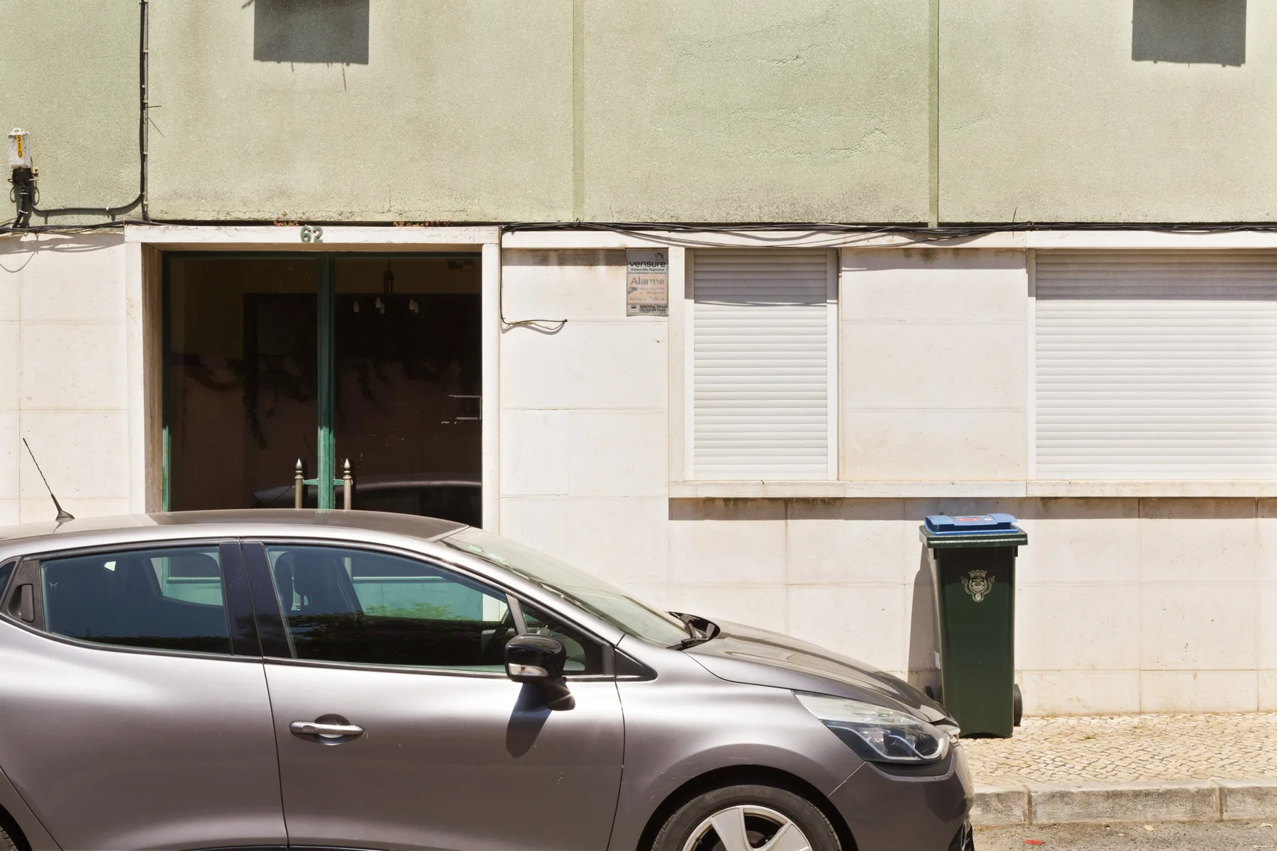 A pale building facade with a ground-floor entrance and a parked car in front.