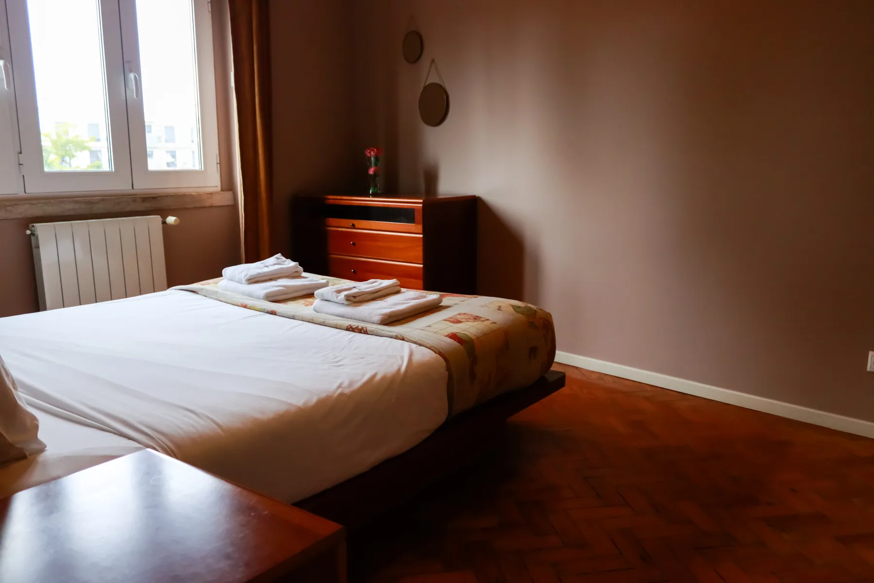 A bedroom with a double bed, folded towels, and a chest of drawers.