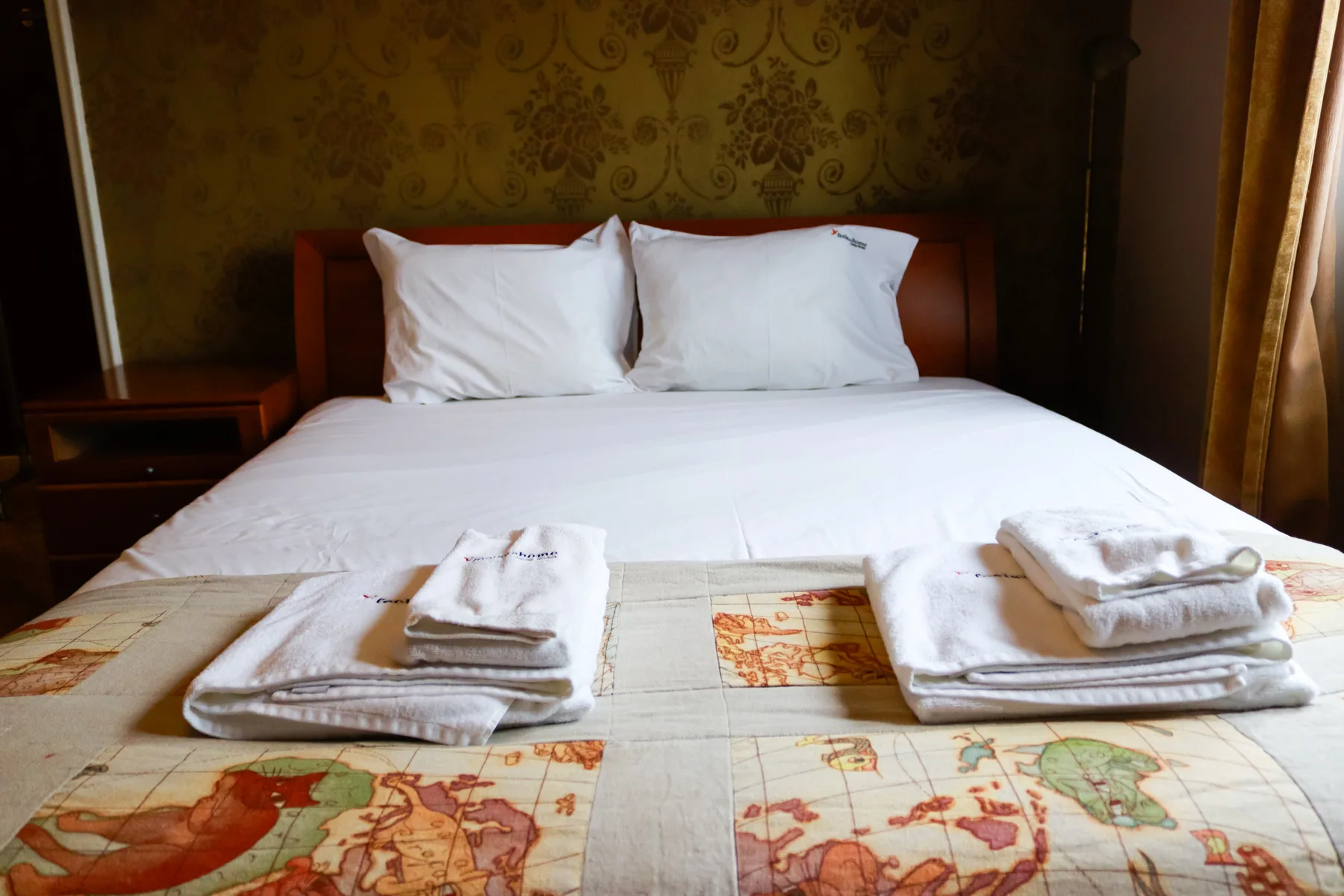 A bedroom with a neatly made bed and folded towels on a map-patterned coverlet.