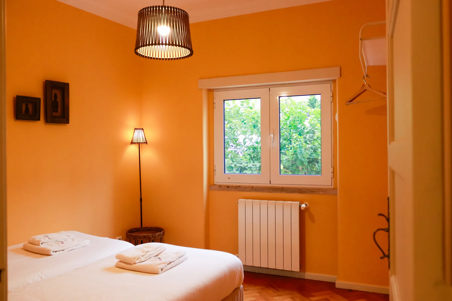 A bedroom with a bed, orange walls, and a window overlooking greenery.