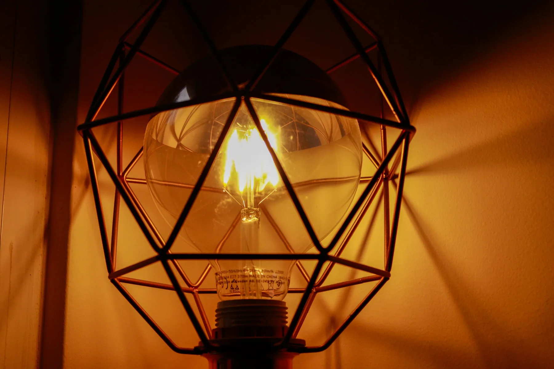 A glowing exposed bulb sits inside a black geometric metal light fixture.