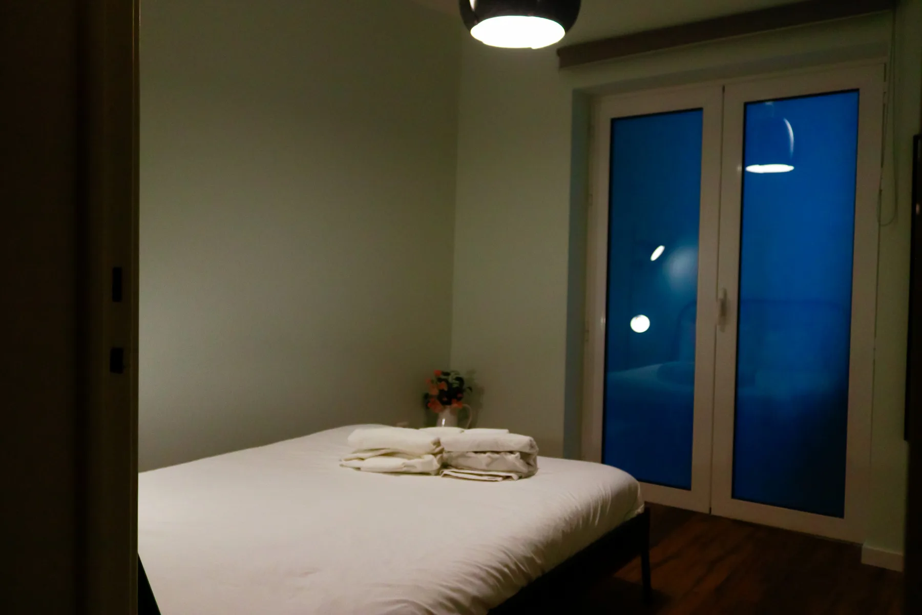 A bedroom with a neatly made bed beside a tall window.