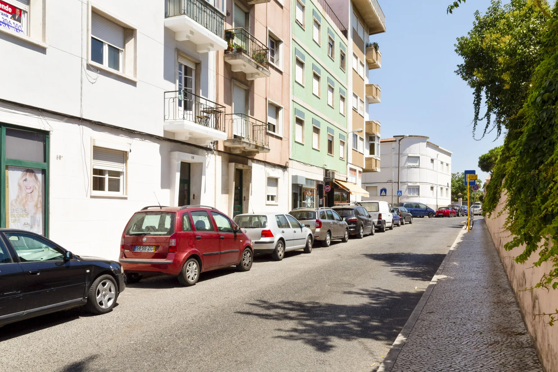 A sunny urban street lined with apartment buildings and parked cars.