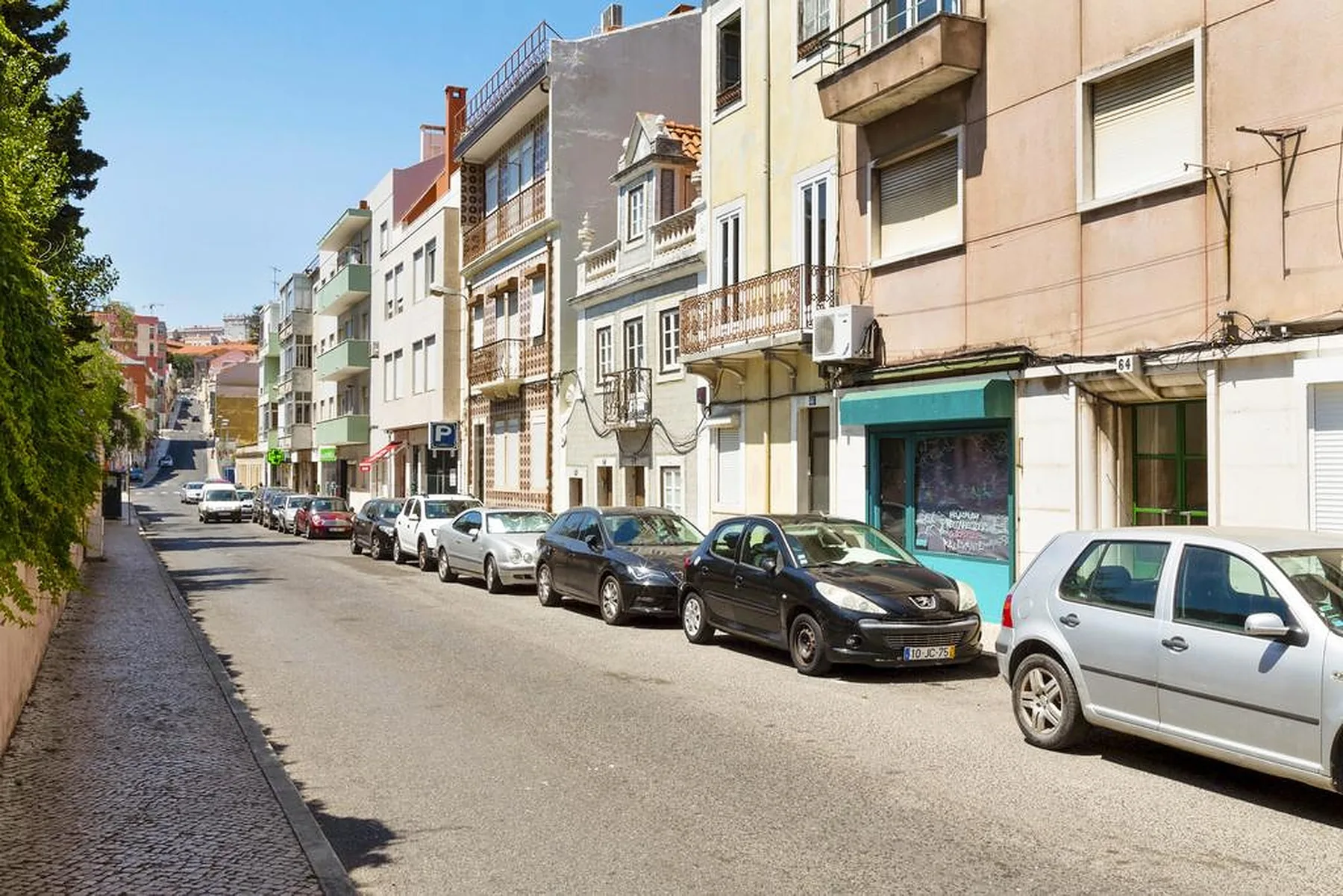 A sunny urban street lined with apartment buildings and parked cars.