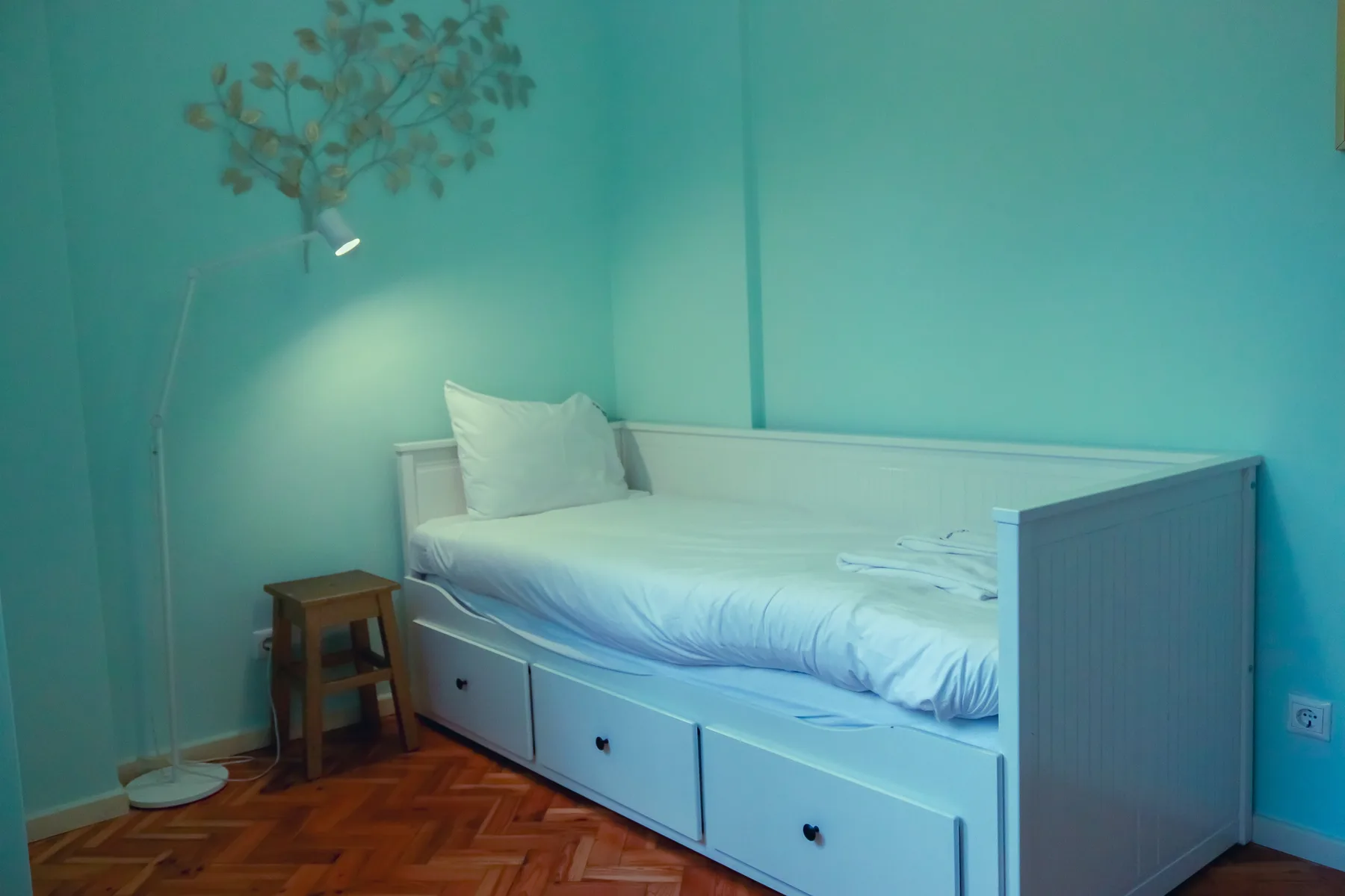 A bedroom with a single bed, storage drawers, and a small side table.