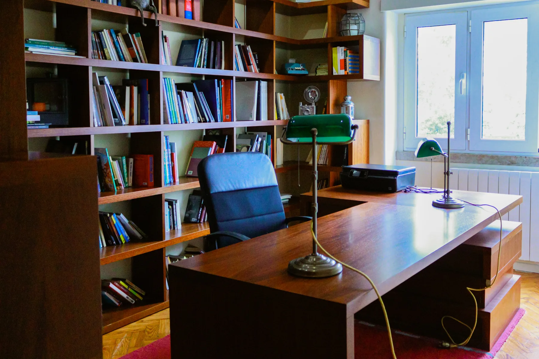 A study with bookshelves, a desk, and a chair beside a window.