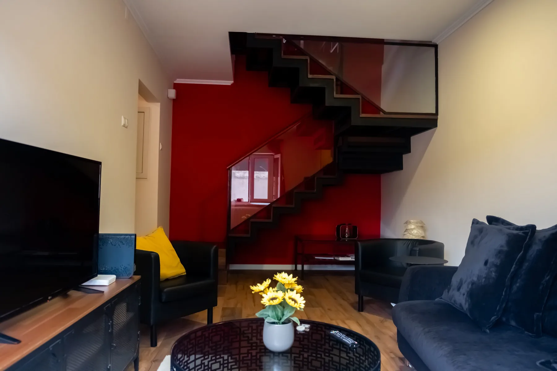 A living room with dark seating and a staircase against a red wall.