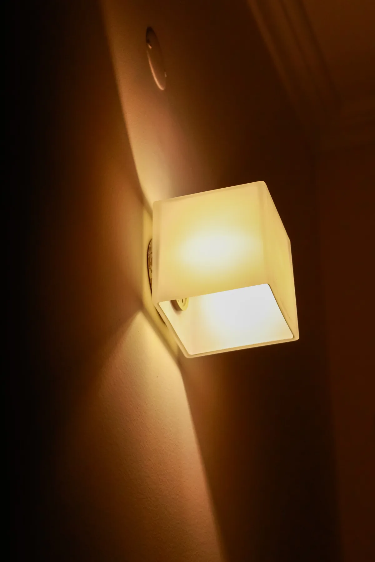 A warm wall light illuminates a dark interior wall.