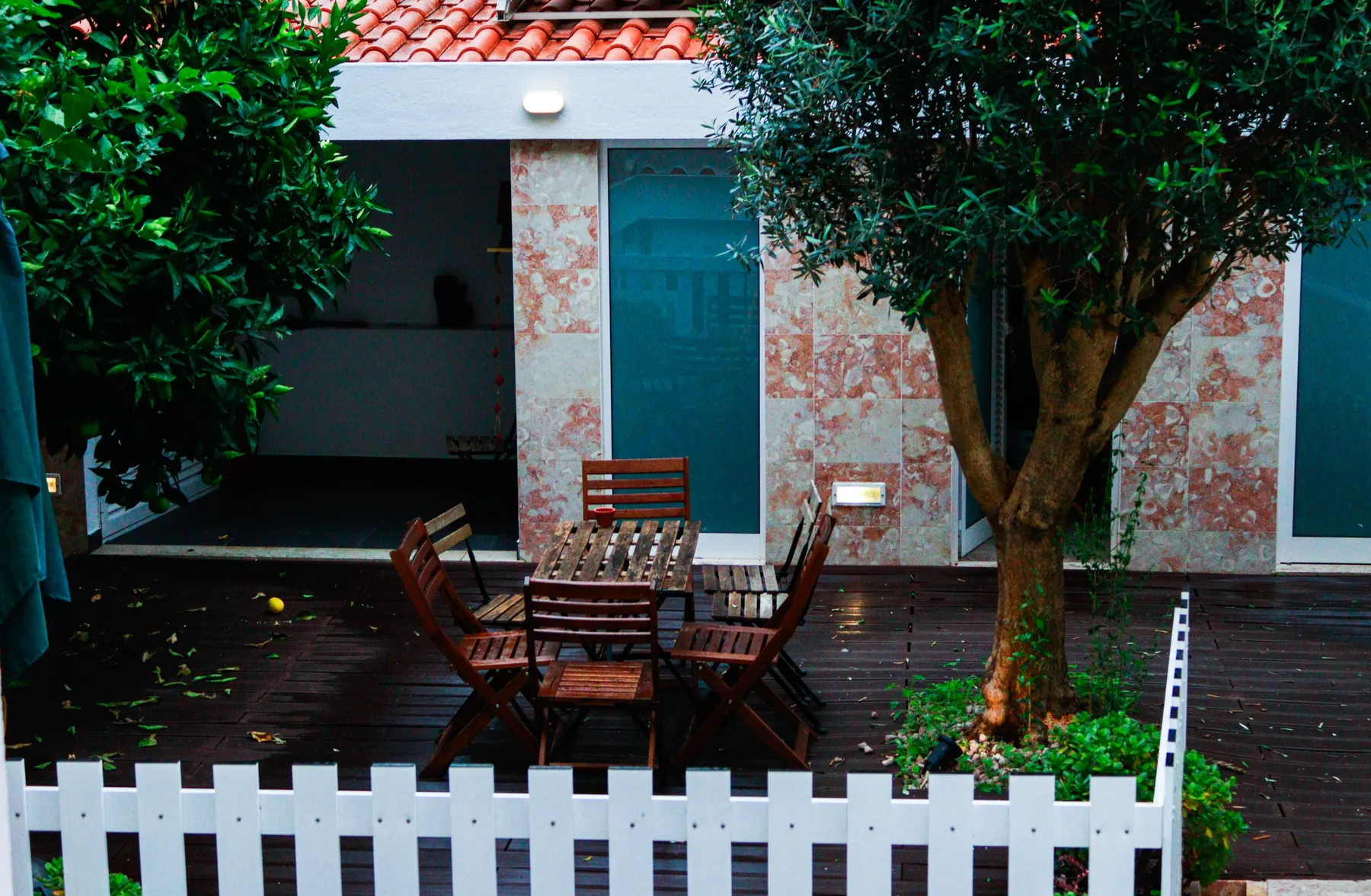 An outdoor patio with wooden seating, trees, and a white fence.