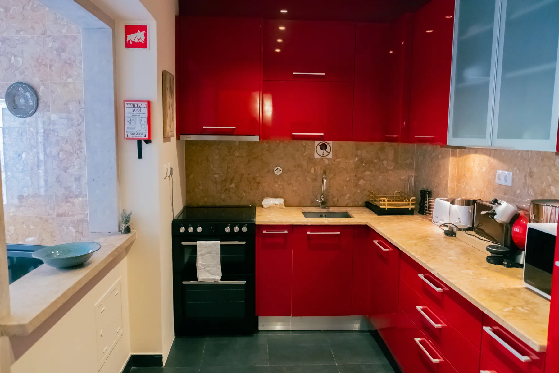 A kitchen with red cabinets, dark countertops, and built-in appliances.