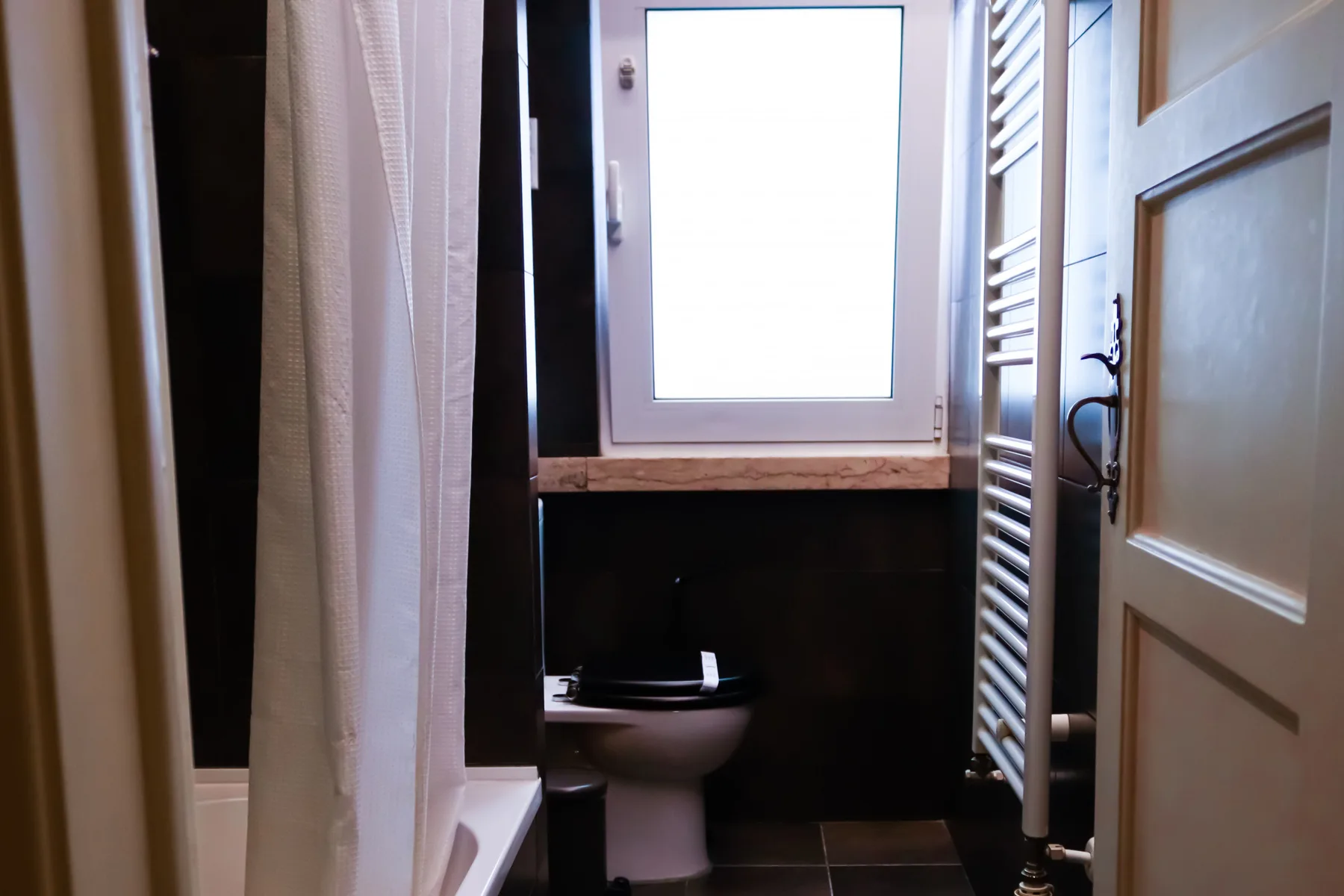 Bathroom with a toilet beneath a window and a shower curtain.