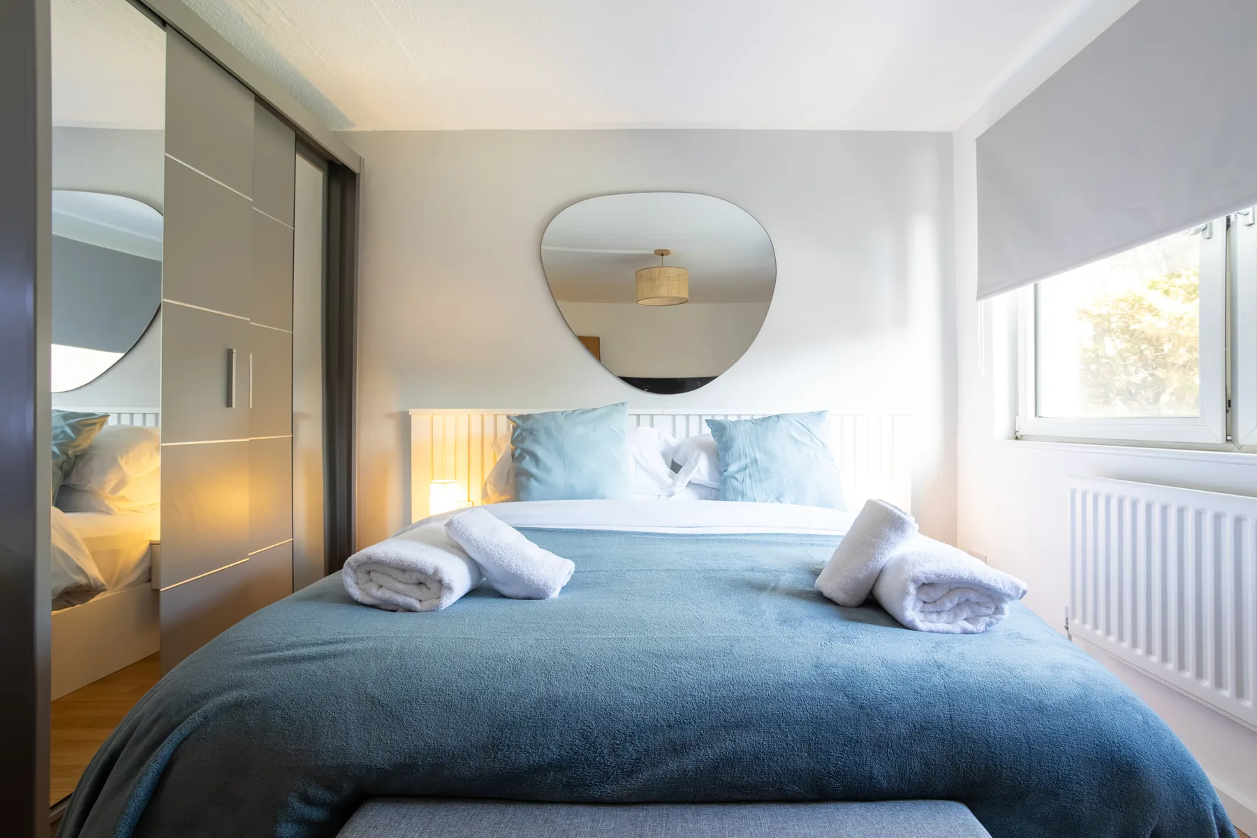 A bedroom with a bed beneath a round wall mirror.