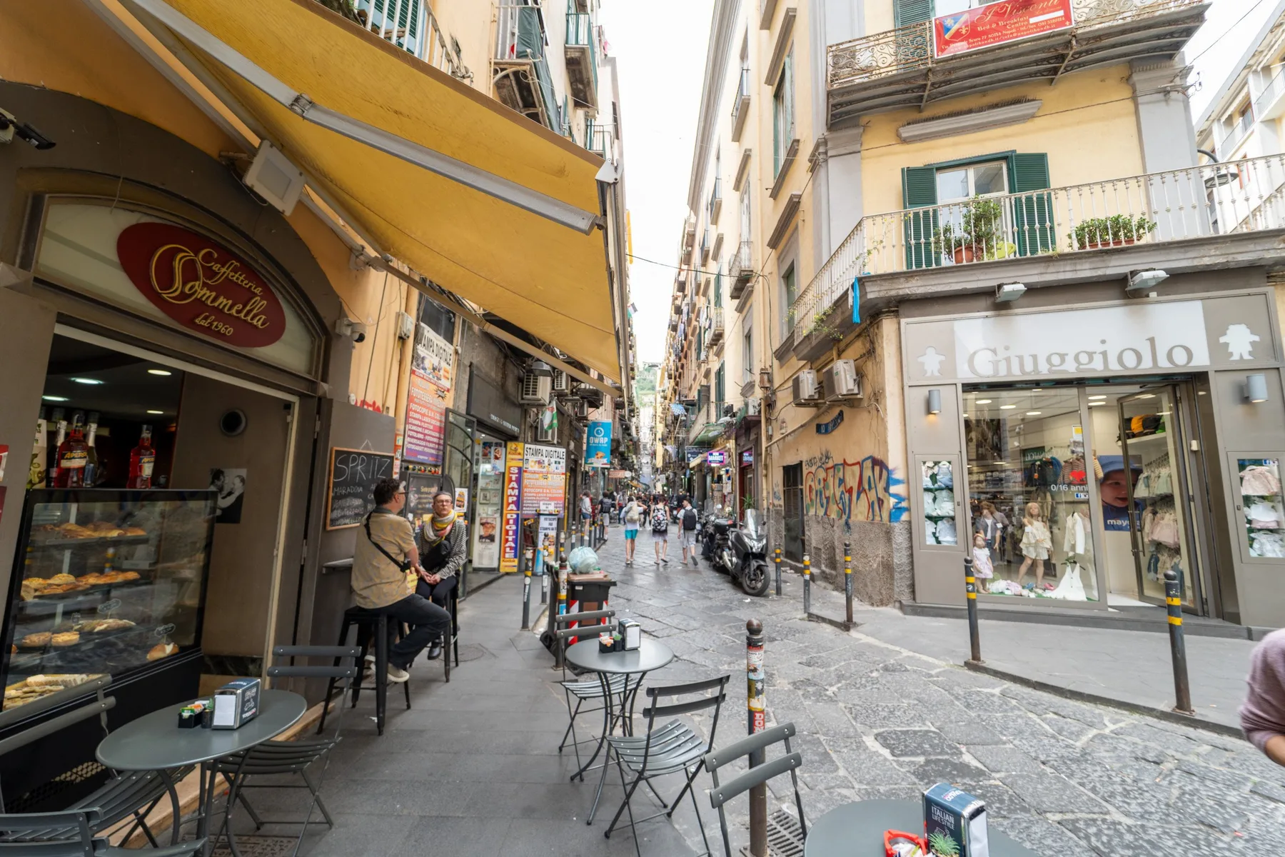 A narrow pedestrian street lined with shops, cafés, and outdoor seating.