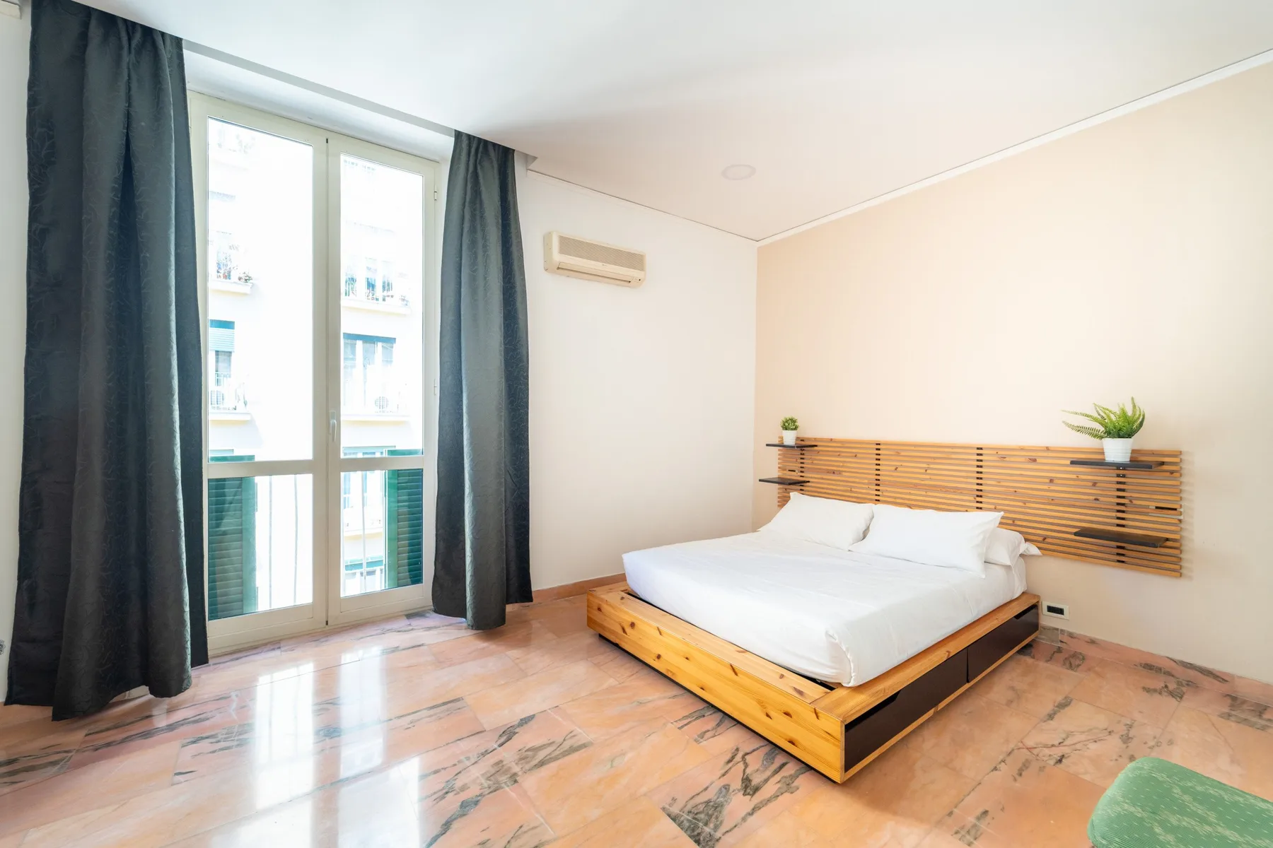 A bedroom with a low bed, wood slat headboard, and tall curtained windows.