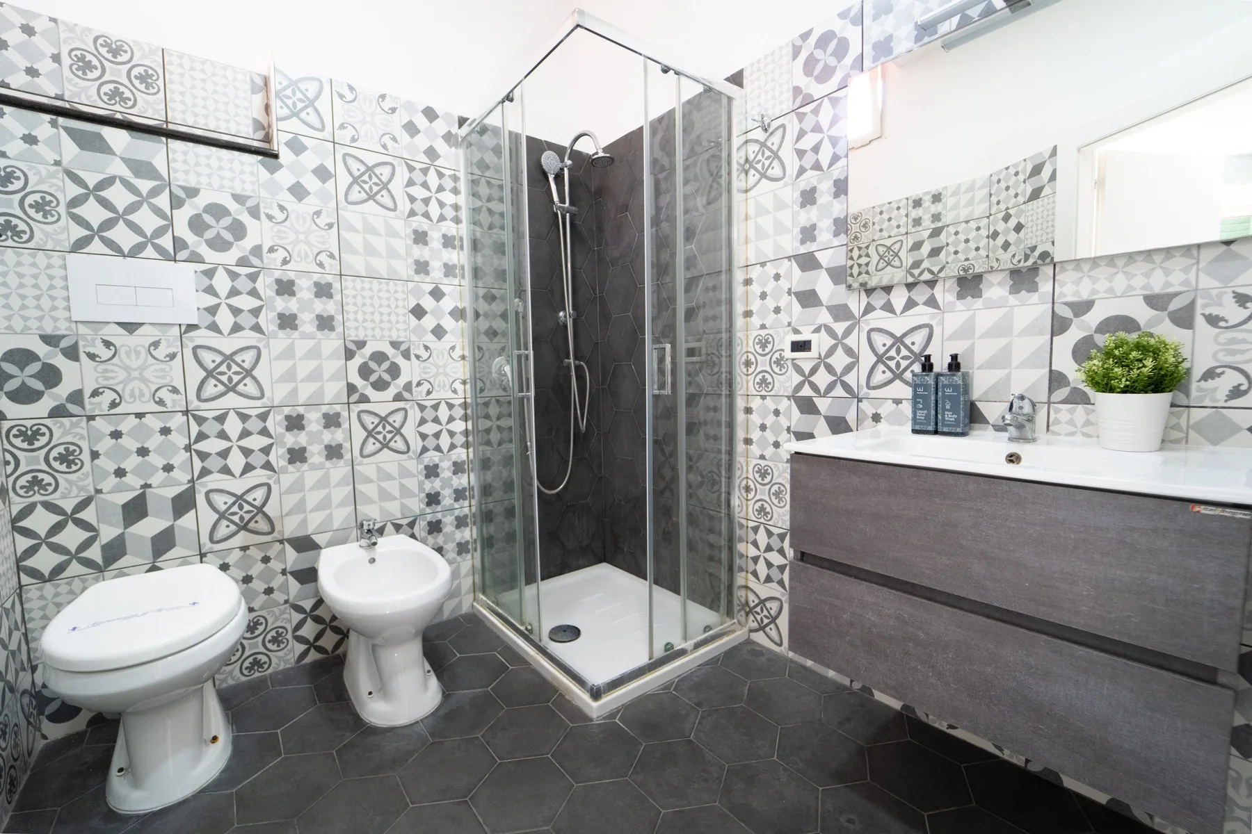 A bathroom with patterned tile, a glass shower, and a vanity.