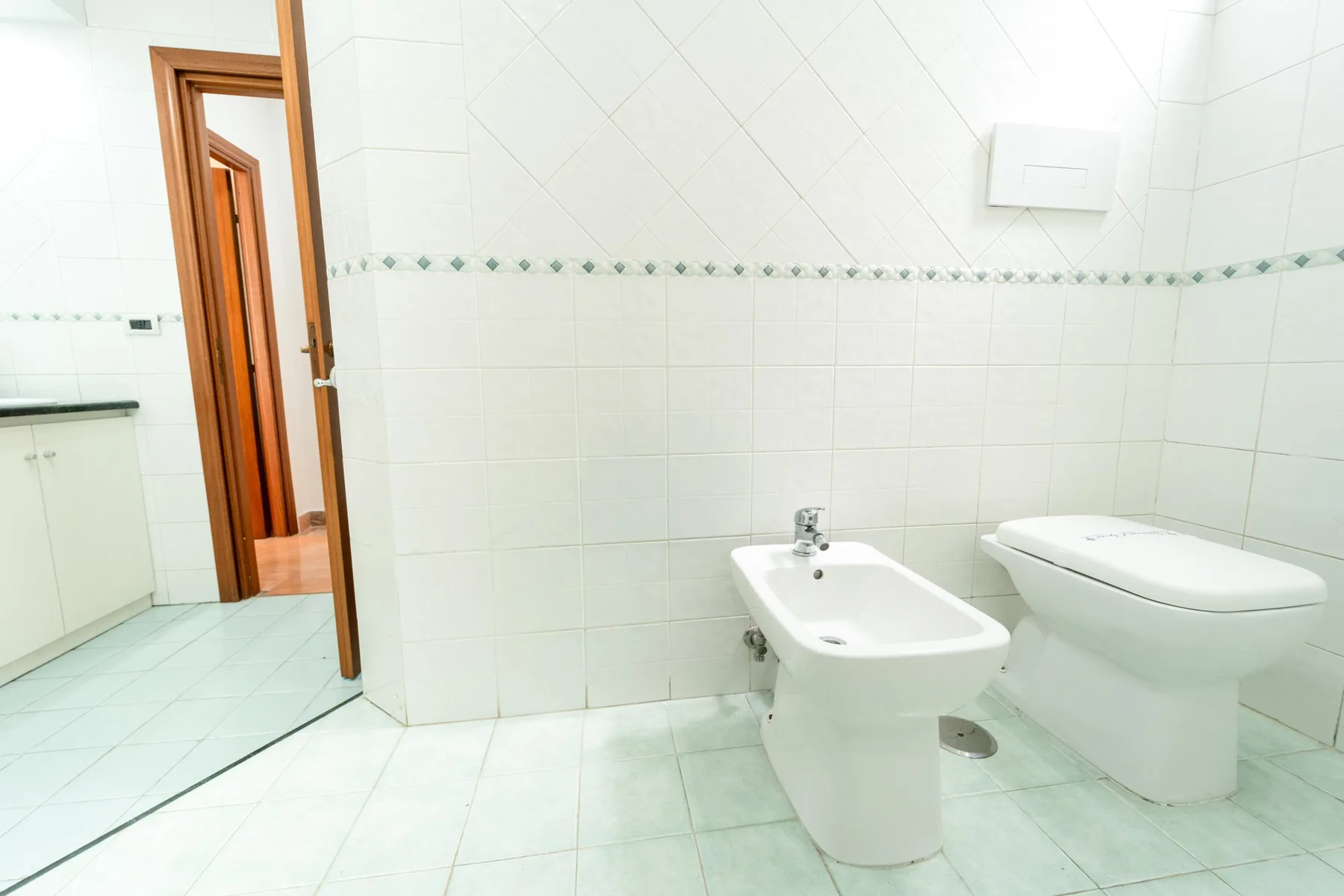 A tiled bathroom with a bidet and toilet beside the doorway.