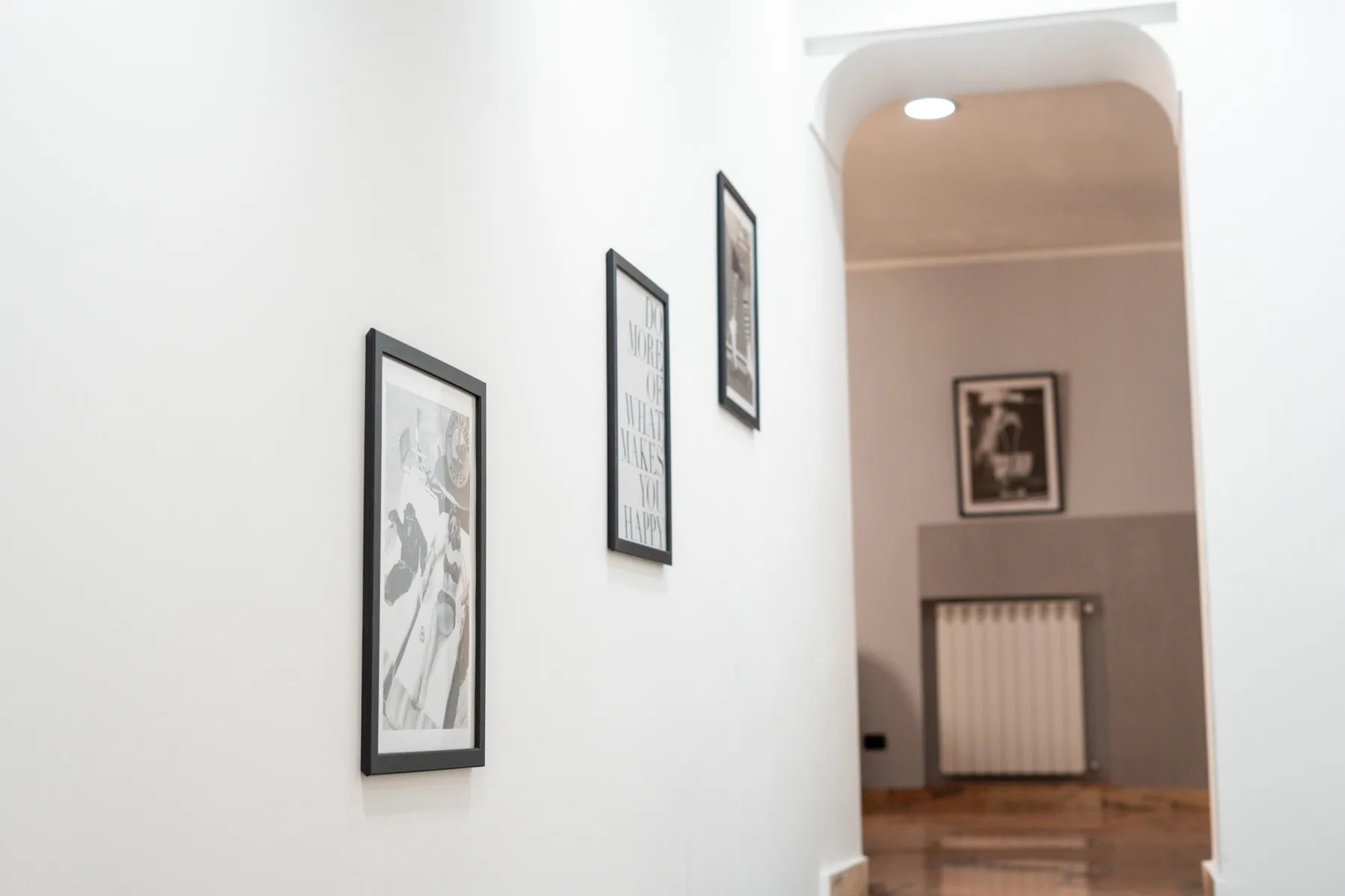 A hallway with framed pictures on the wall and a radiator at the far end.