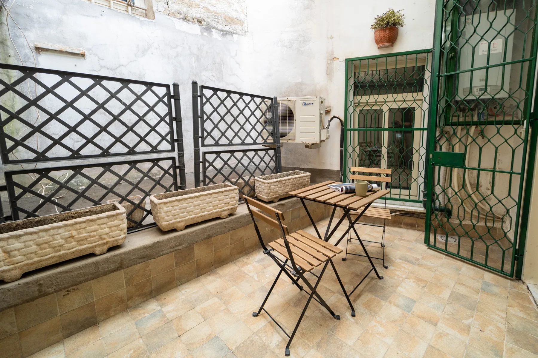 A tiled patio with folding seating and planters beside a green metal gate.