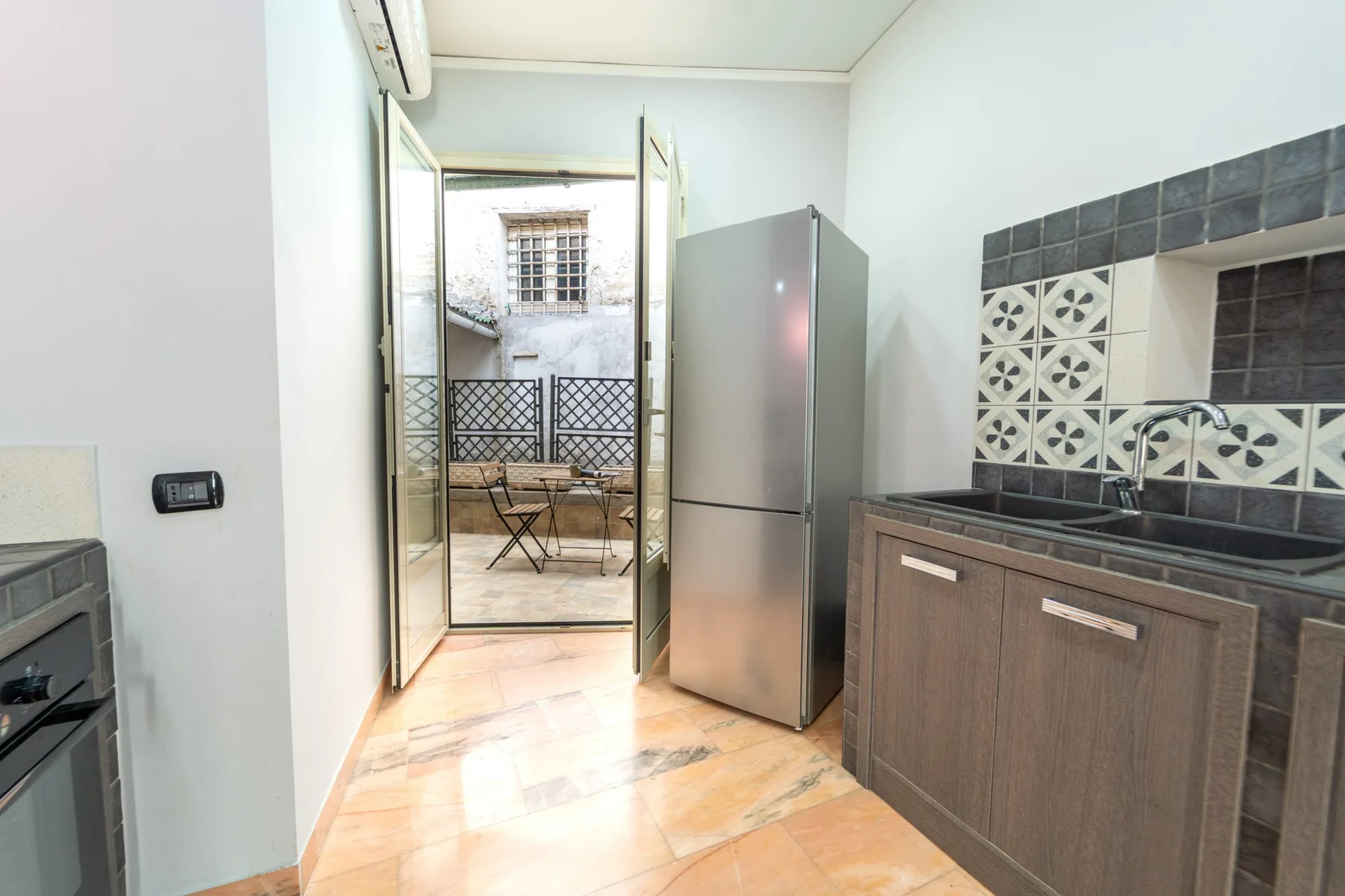 A kitchen with a refrigerator and a counter beside an open balcony door.