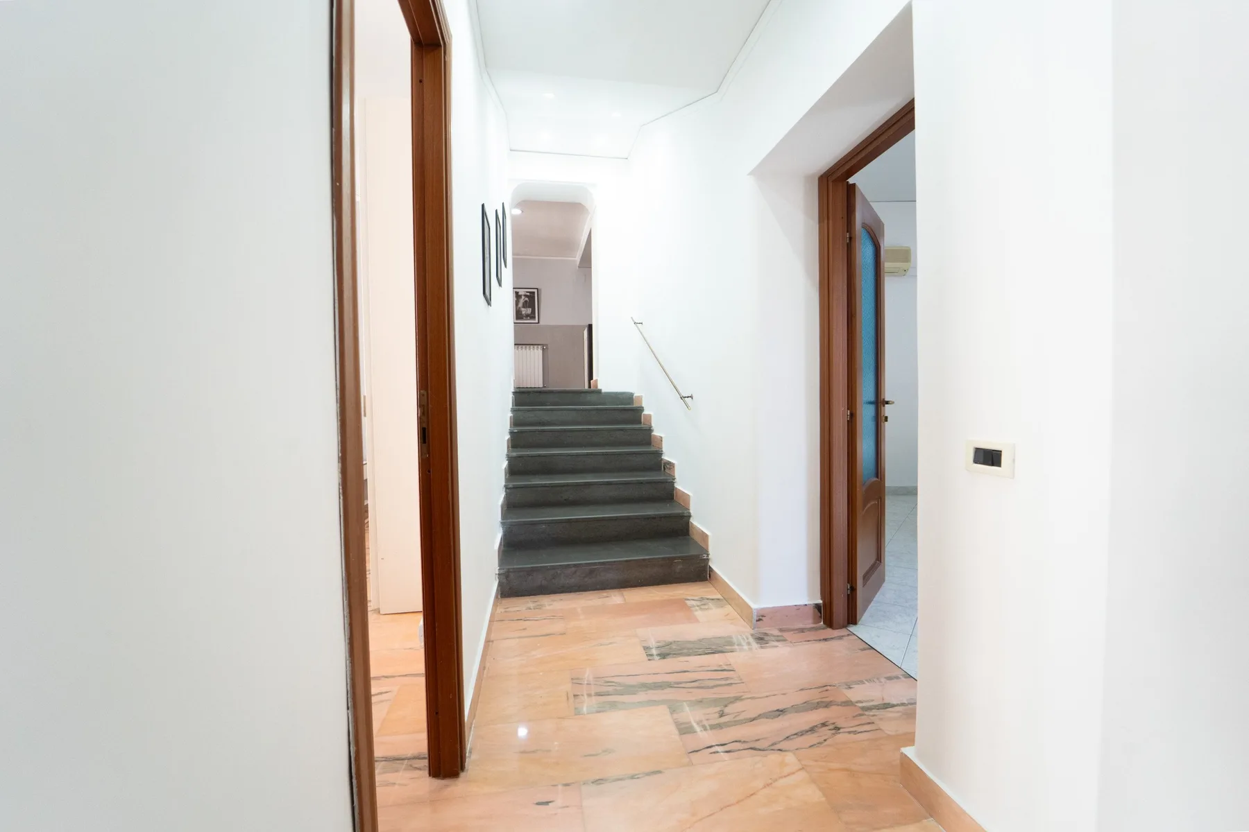 A bright hallway leads to a staircase, with wooden doors along the corridor.