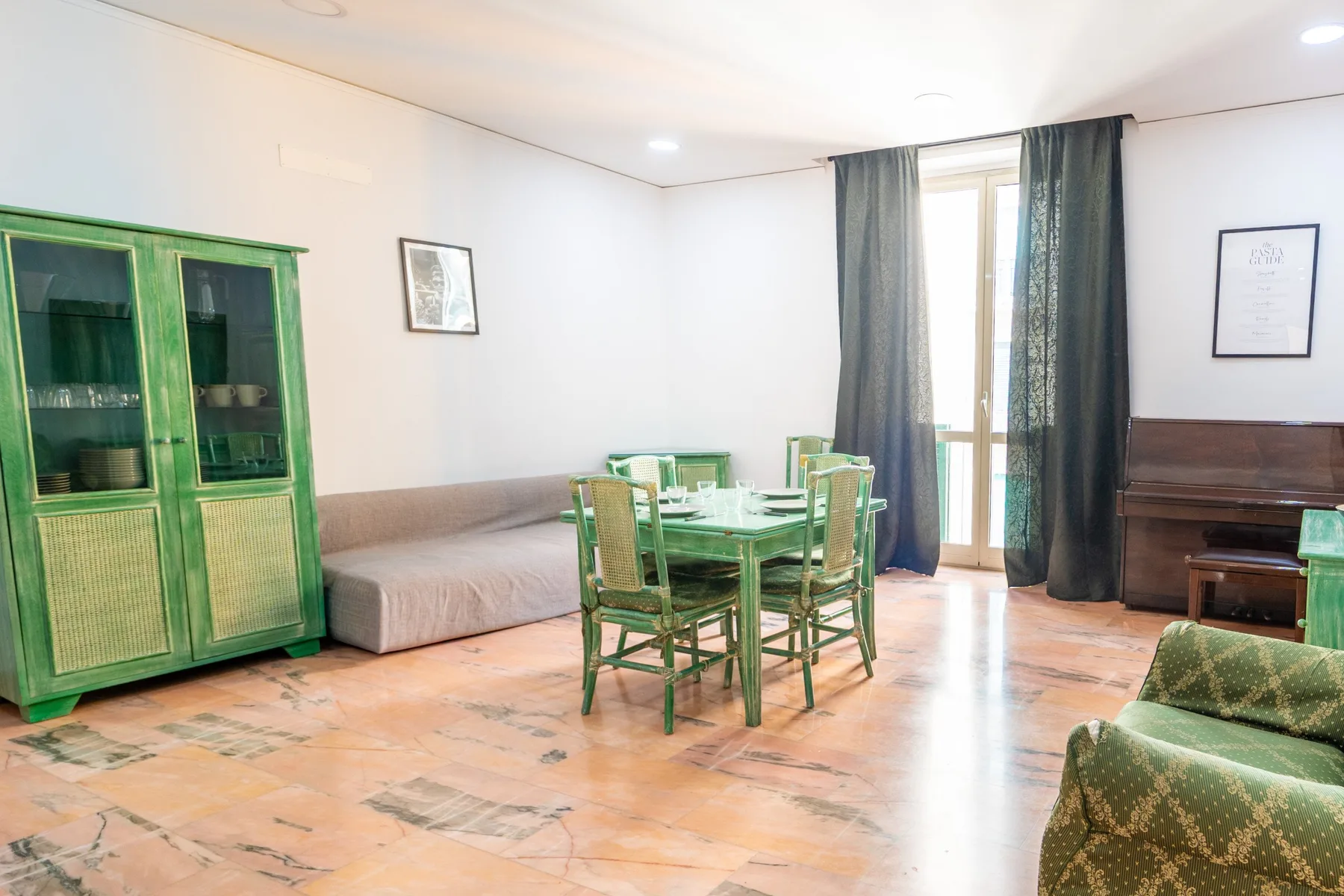 A dining area with green seating and a glass-front cabinet beside tall curtained windows.