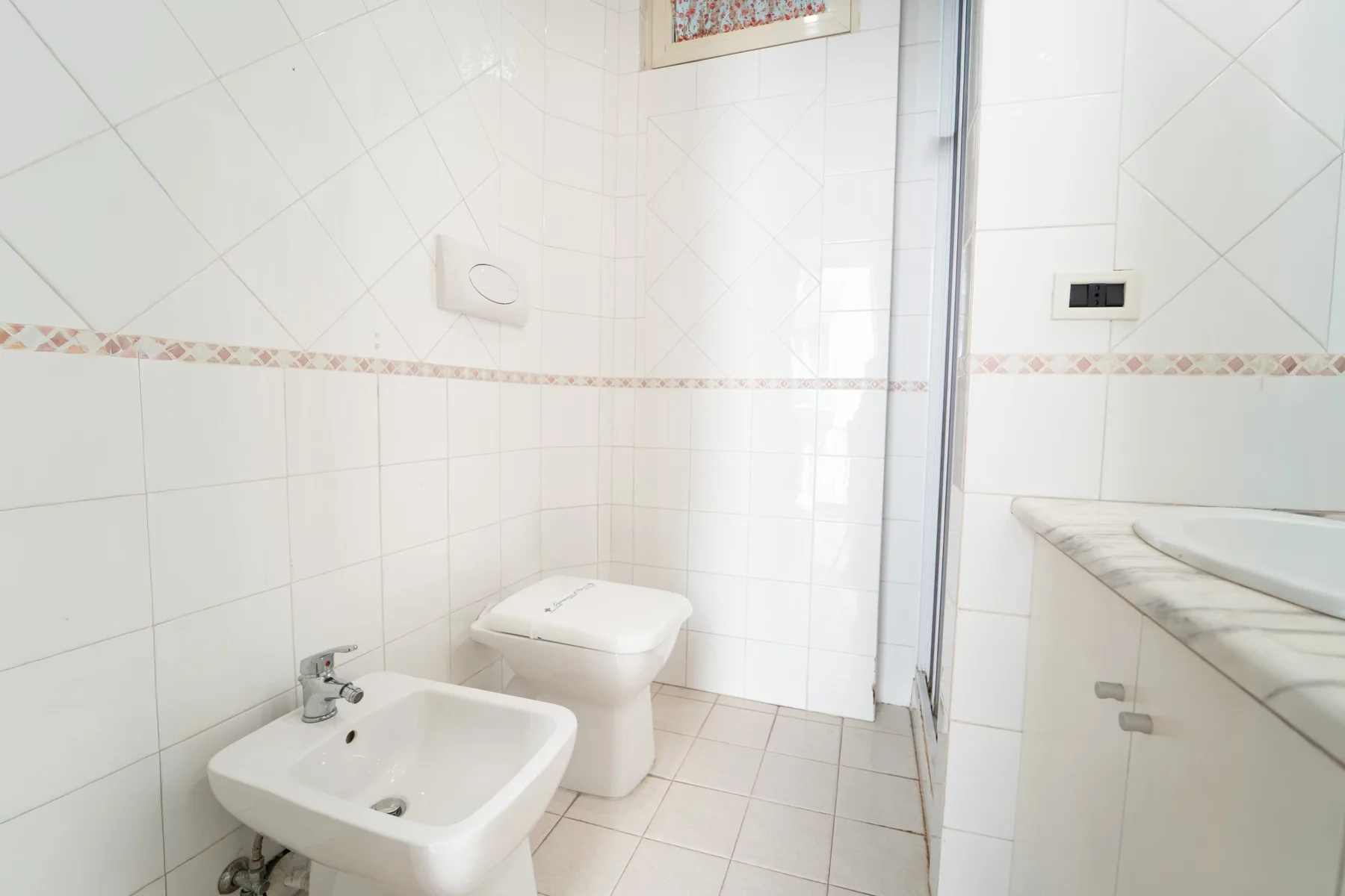 A tiled bathroom with a toilet, wall-mounted sink, and bathtub.
