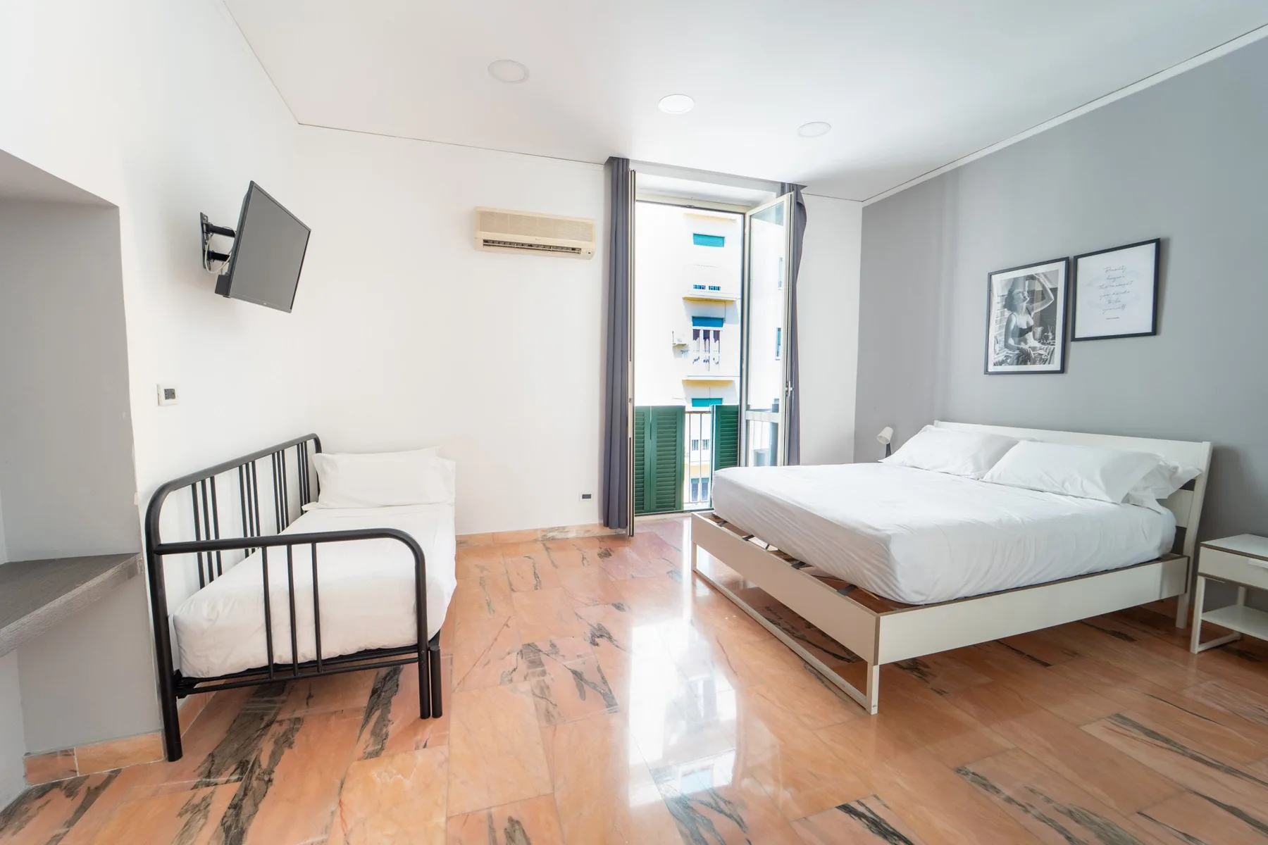 A bedroom with a large bed, a single bed, and a doorway opening to a balcony.